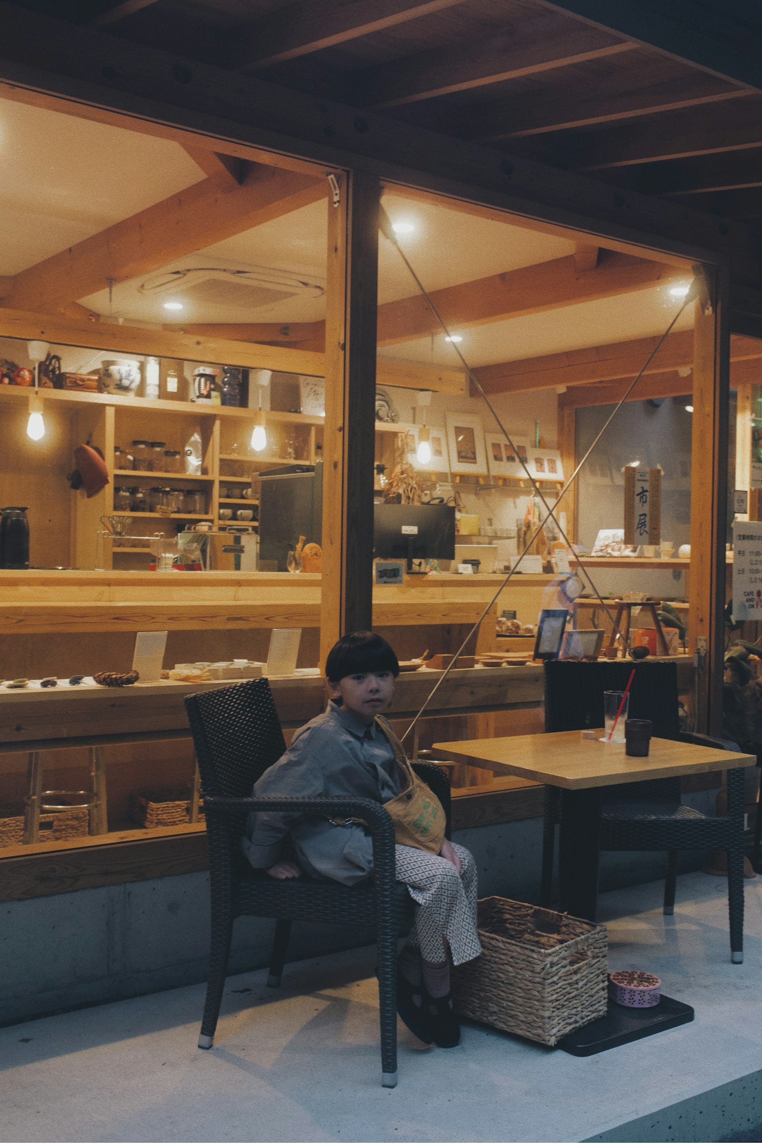 Kind sitzt draußen vor einem Café mit warmem Holzinterieur und sanfter Beleuchtung