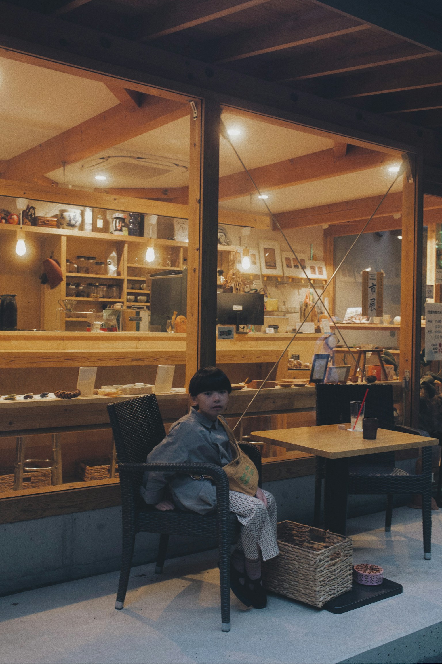 Child sitting outside a cafe with warm wooden interior and soft lighting