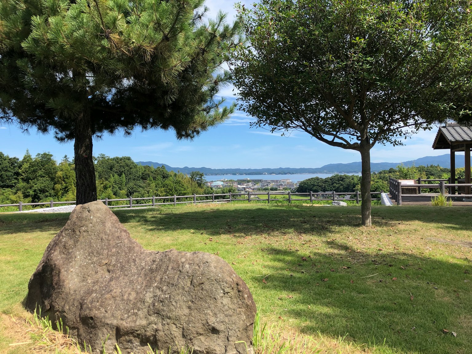 Großer Stein in einem Park mit zwei Bäumen und einer fernen Landschaft