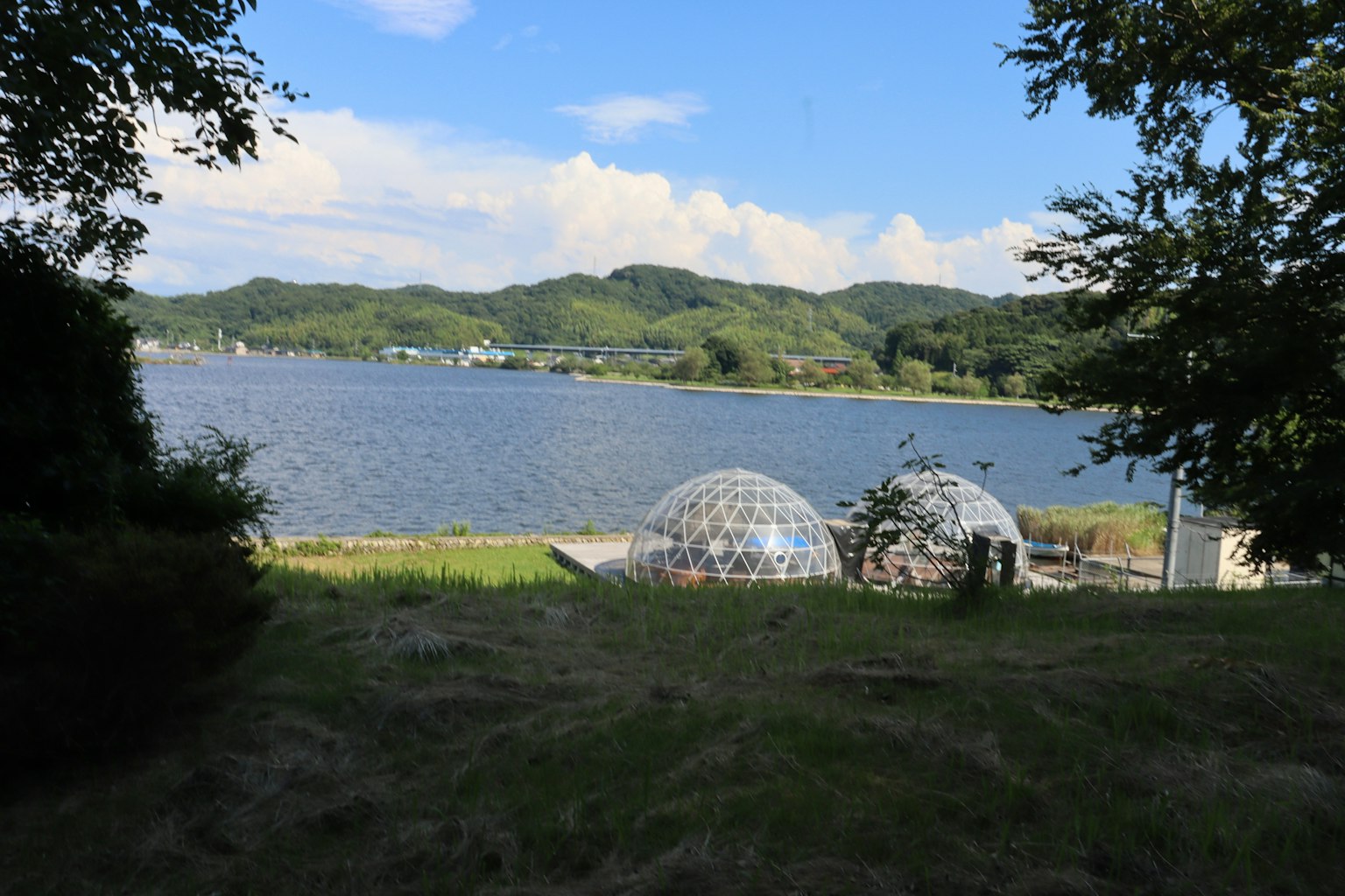 Scenic view of transparent domes by a lake surrounded by green hills