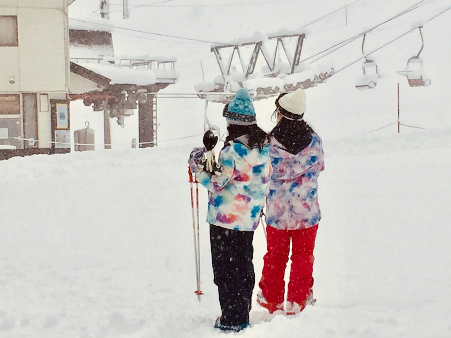 Two women in colorful jackets waiting in the snow at a ski resort