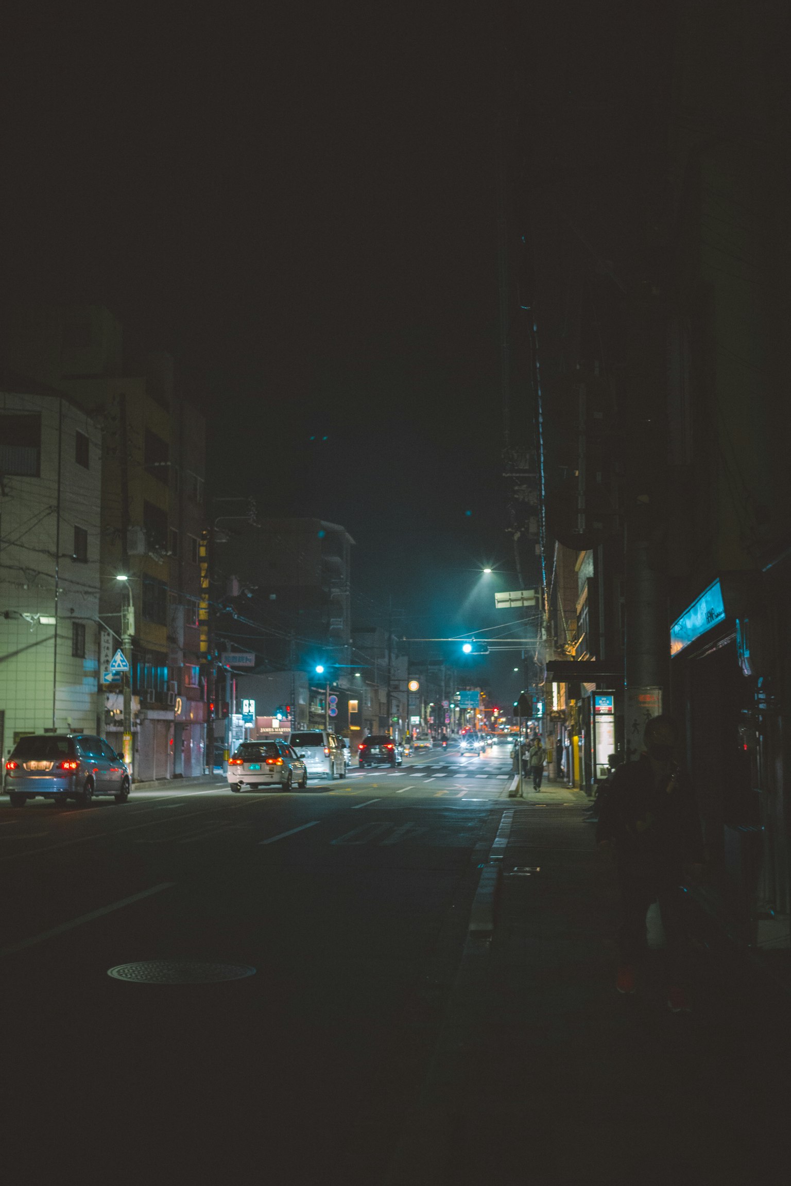 Paesaggio urbano notturno con semaforo blu, luci delle auto, edifici, strada tranquilla