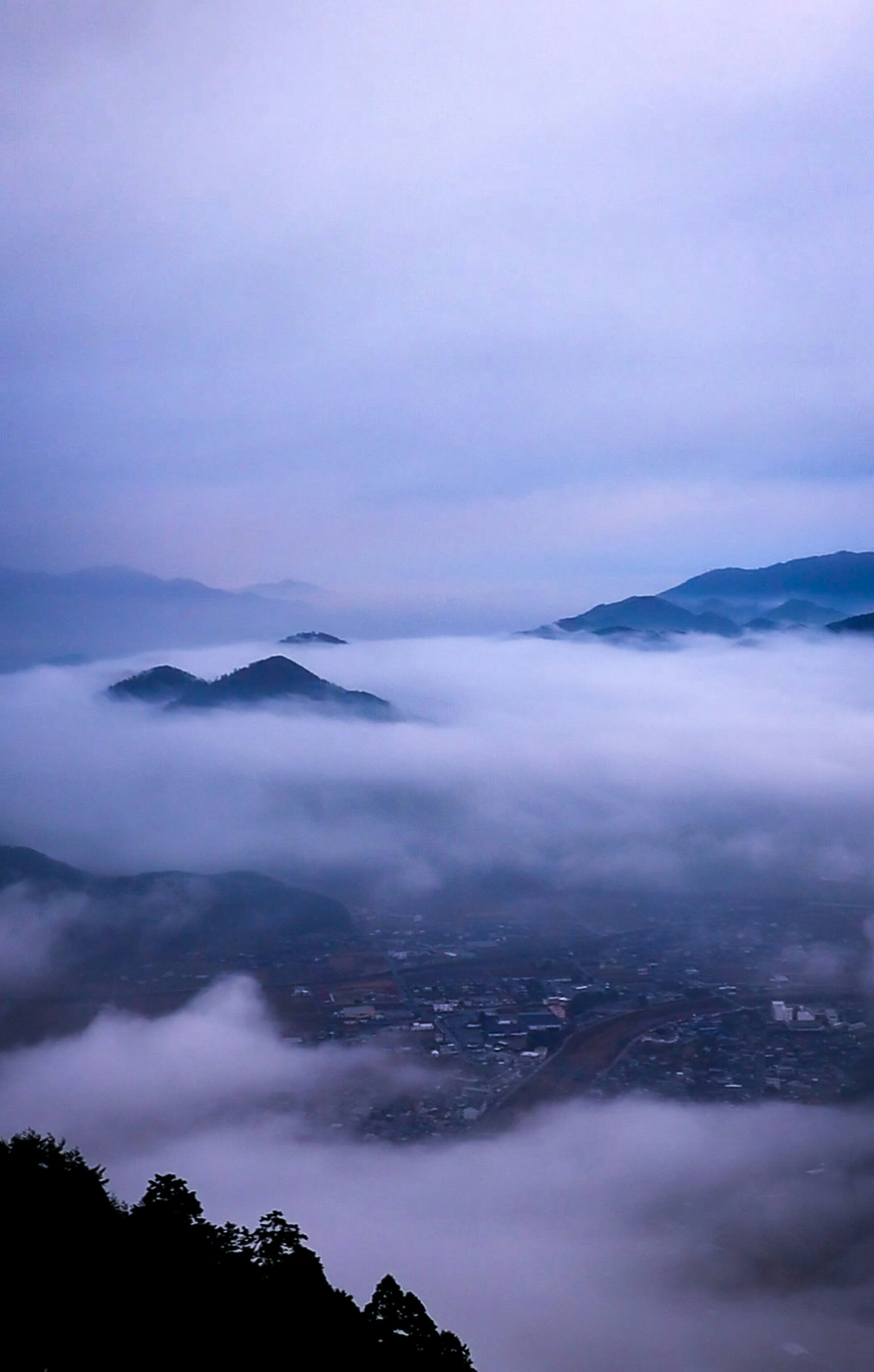 mountain ridges and a city below seen through a sea of clouds at dawn