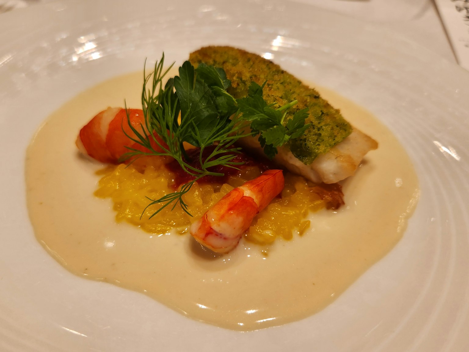 A beautifully plated dish featuring a fish fillet topped with green herbs and shrimp