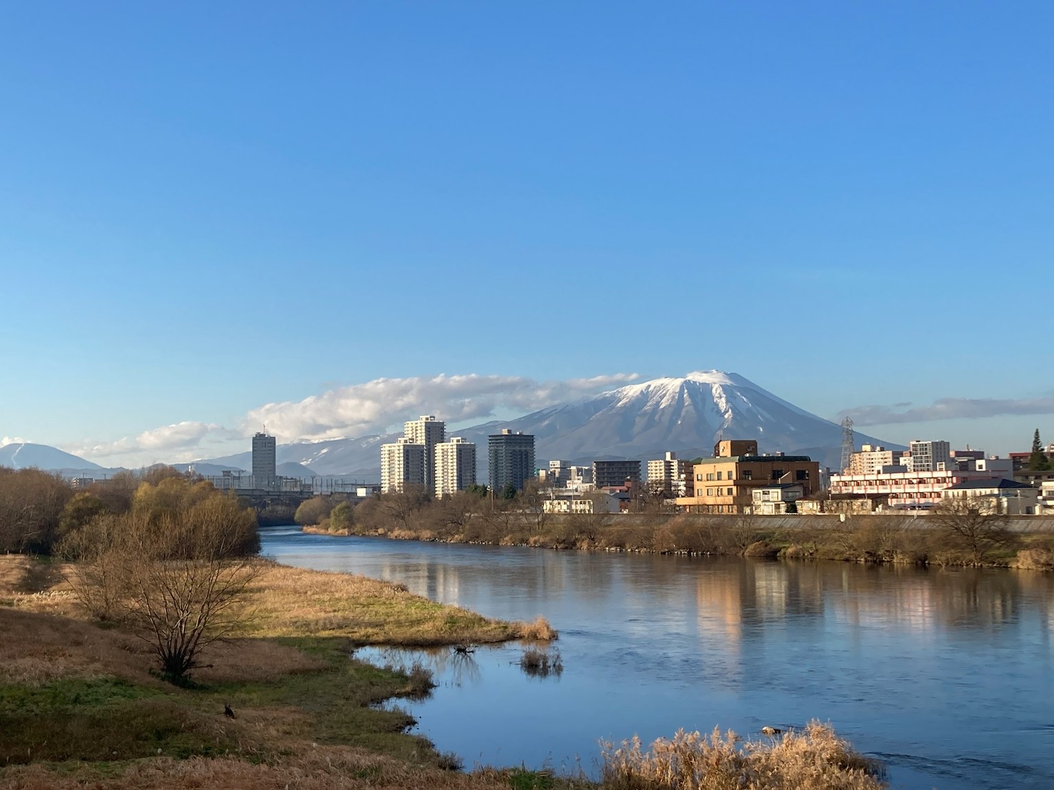 在明亮蓝天下的河流景观，岸边有城市建筑，背景是雪山