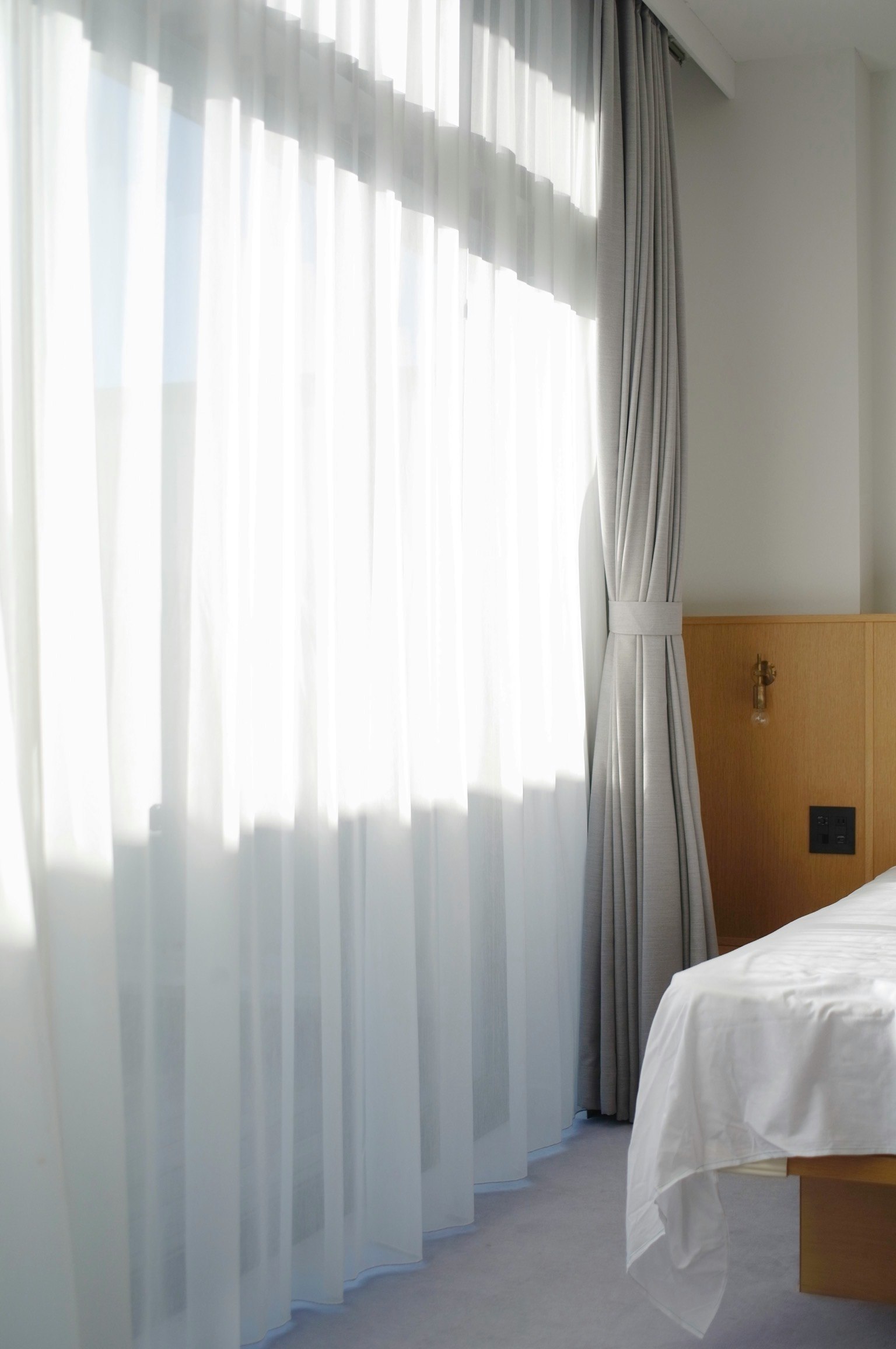Tende chiare in una camera da letto semplice con un letto e testiera in legno
