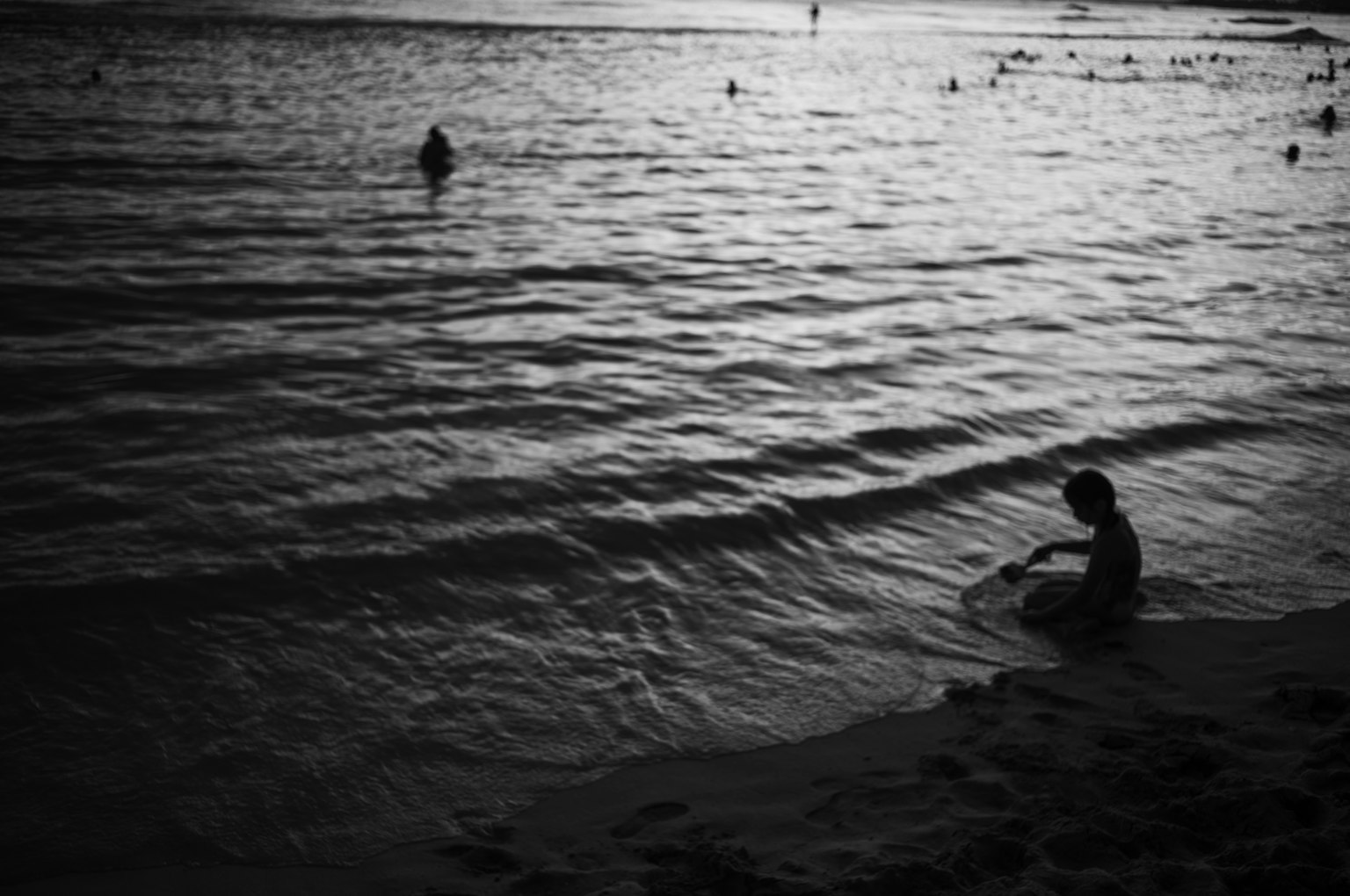 Enfant jouant sur la plage avec des vagues en noir et blanc