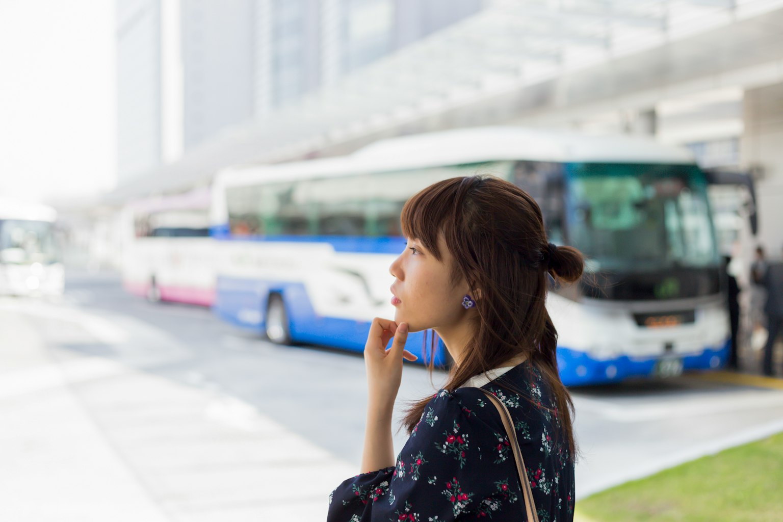 一位女性在公交车站沉思，背景有公交车和城市风景
