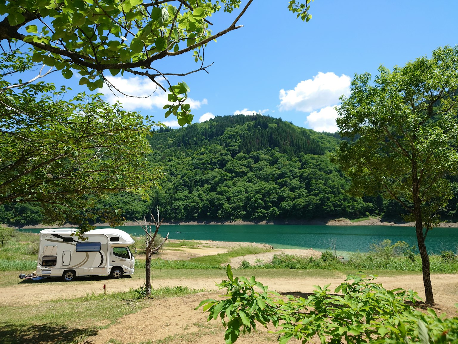 Vista panoramica di un camper vicino a un lago blu e montagne verdi