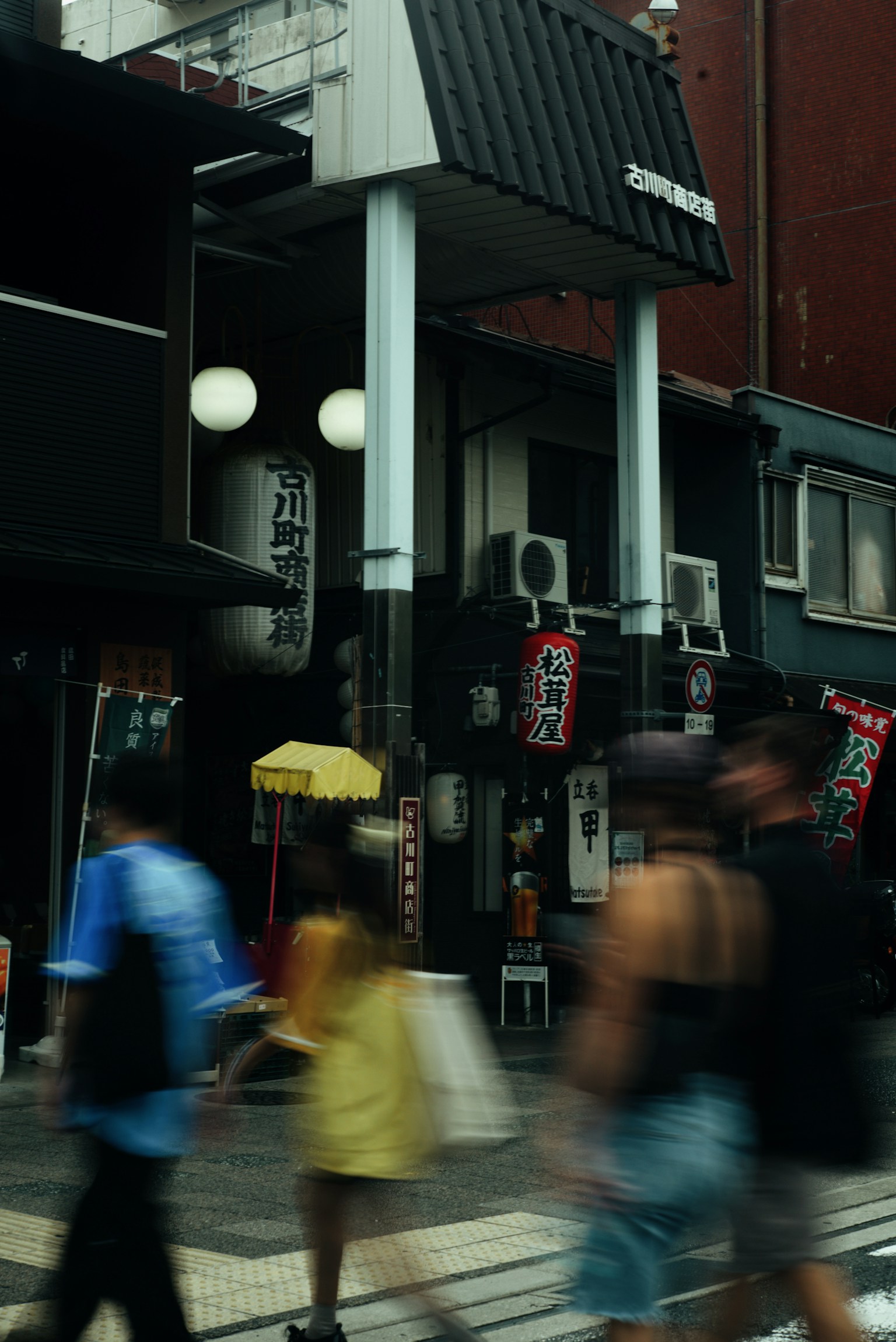 Busy street scene with people walking by featuring a black building and white lamps