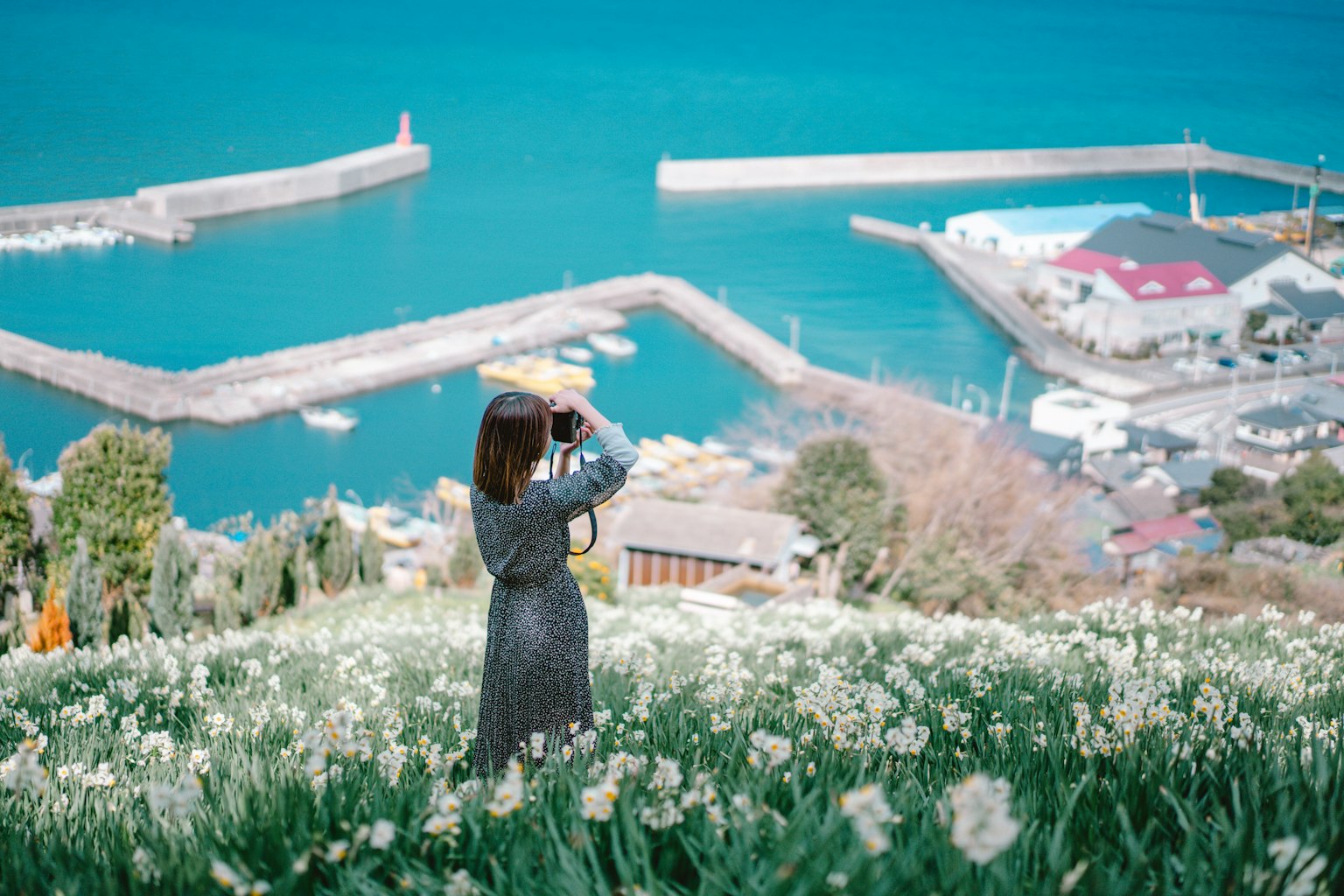 Woman holding a camera in a flower field overlooking the blue sea