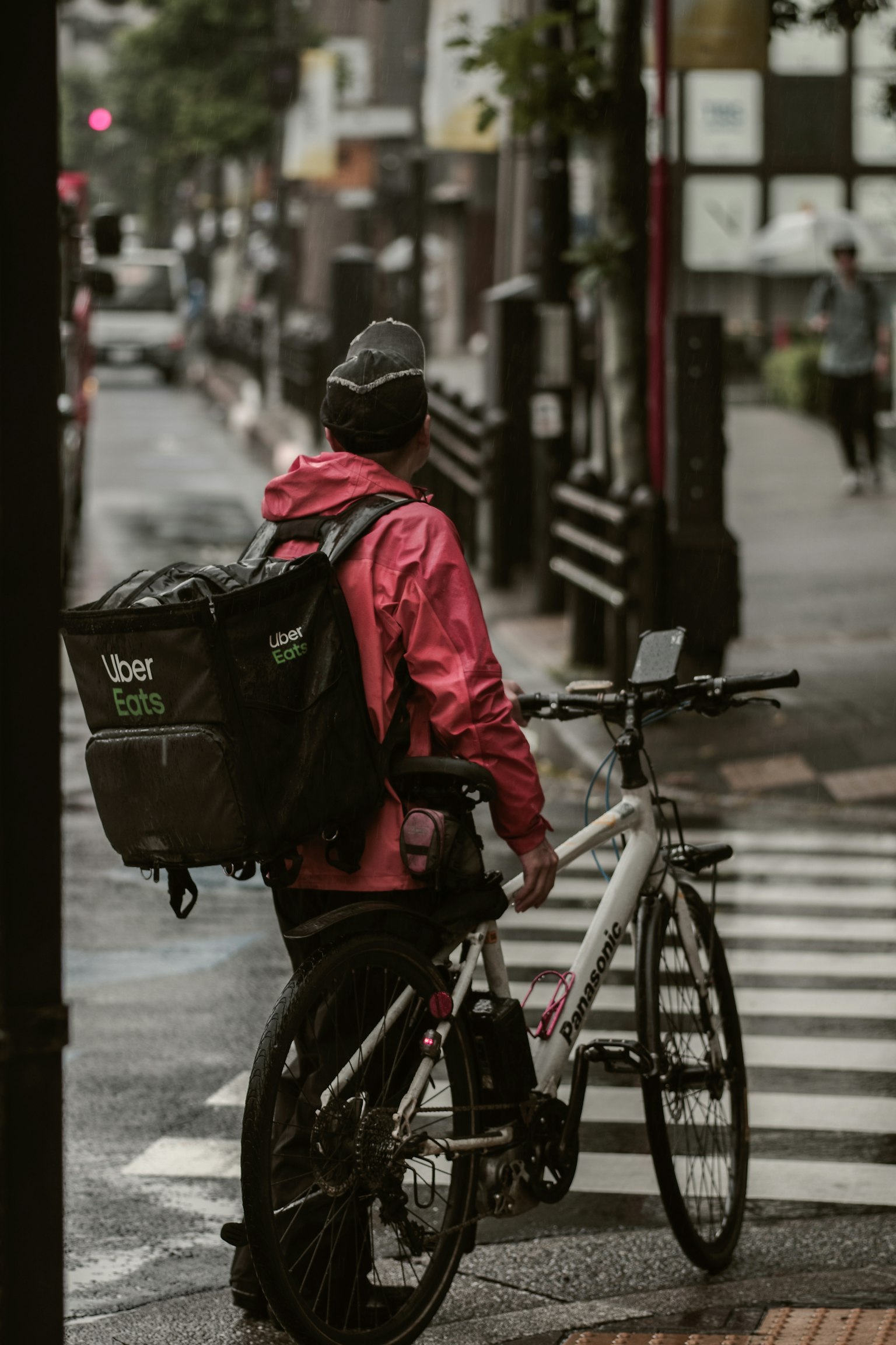 Un livreur à vélo en veste rouge se tenant à un passage piéton avec un vélo