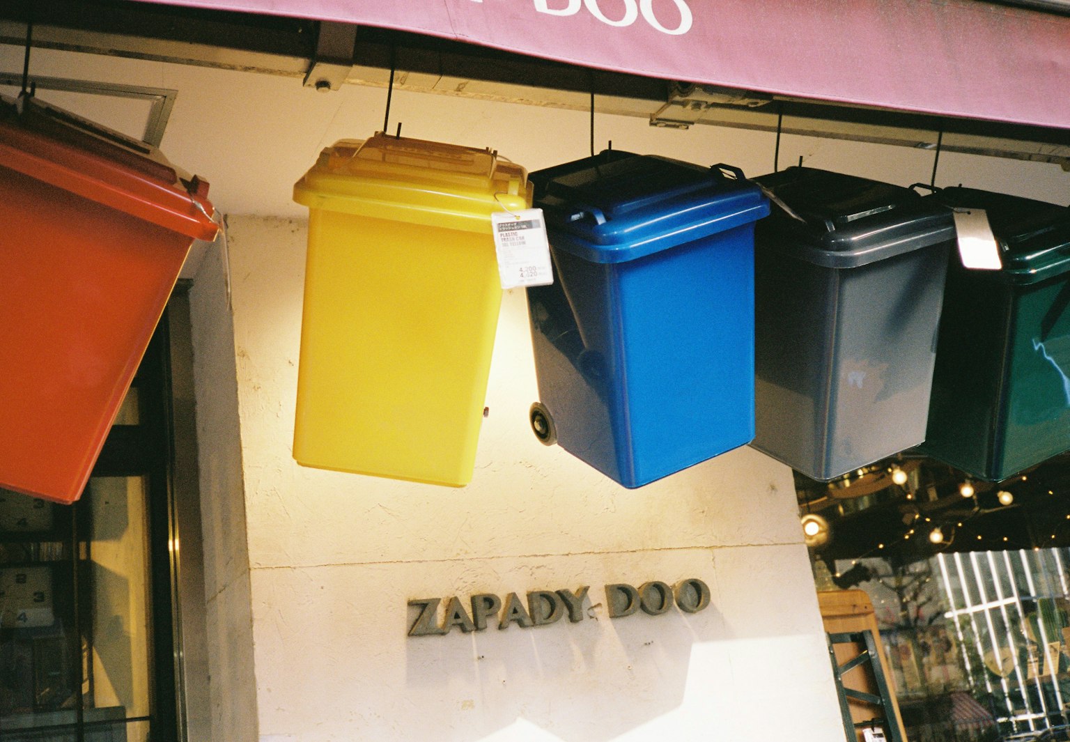 Bidoni colorati appesi all'esterno di un negozio con il cartello Zapady-Doo