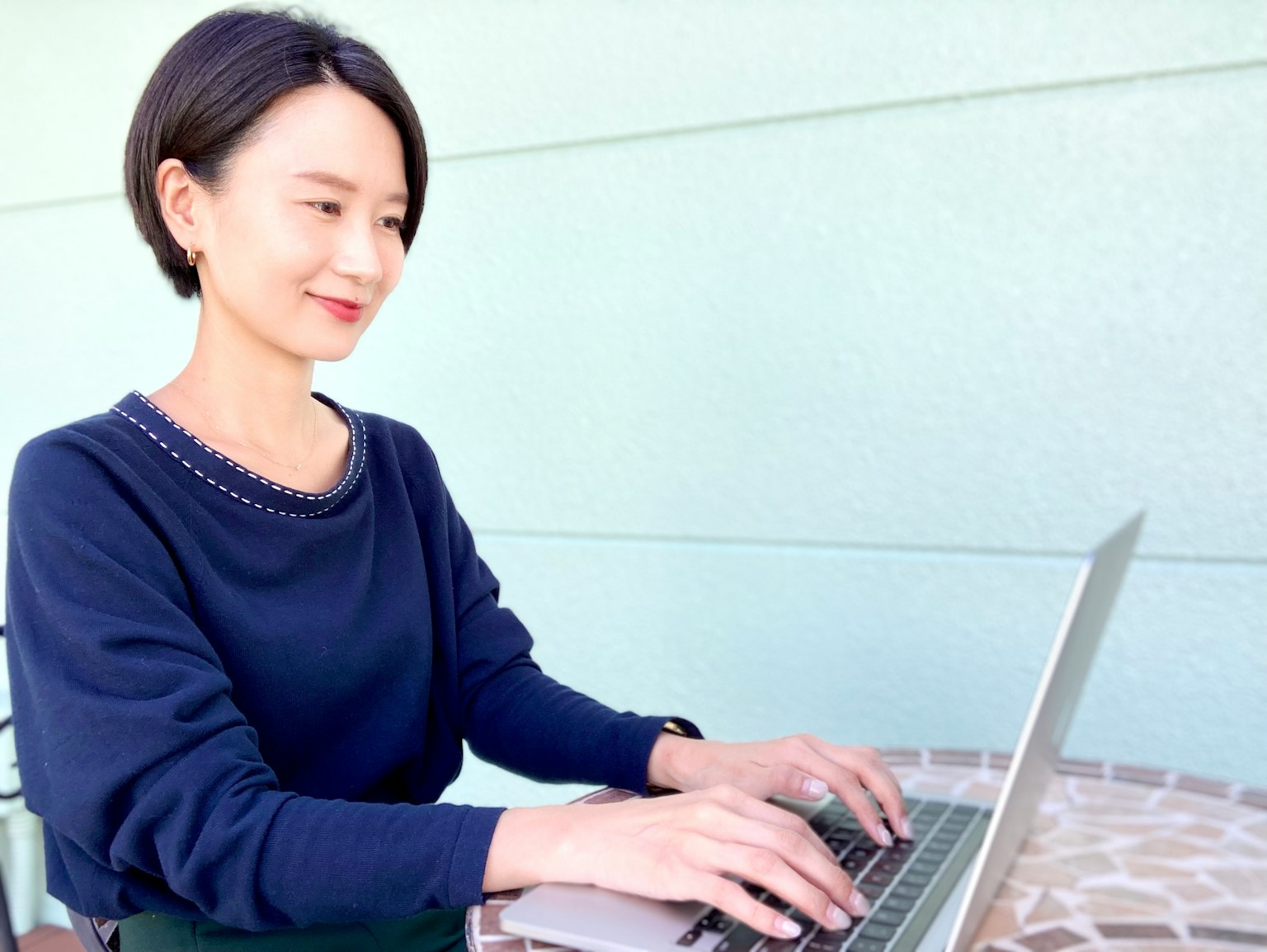 Frau arbeitet im Freien an einem Laptop mit einer hellen Wand im Hintergrund