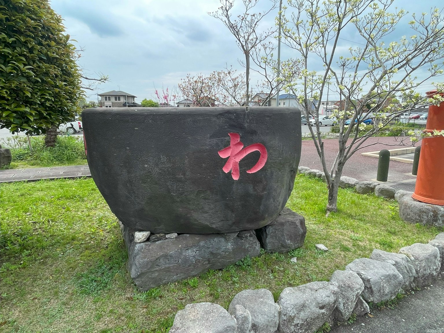 Scultura in pietra nera con carattere rosso 'わ' in un parco