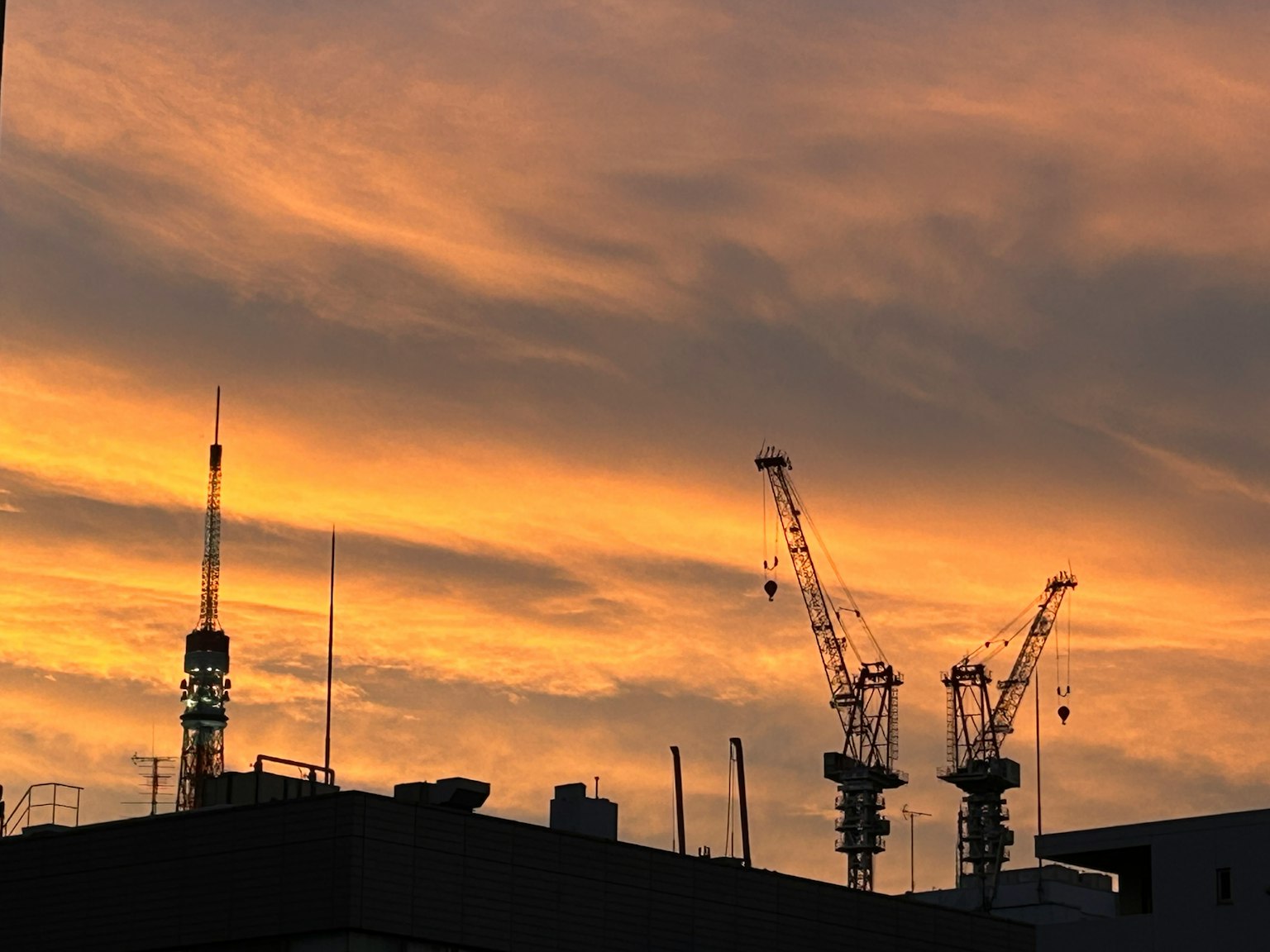 Kran dan menara komunikasi bersiluet di latar belakang langit senja