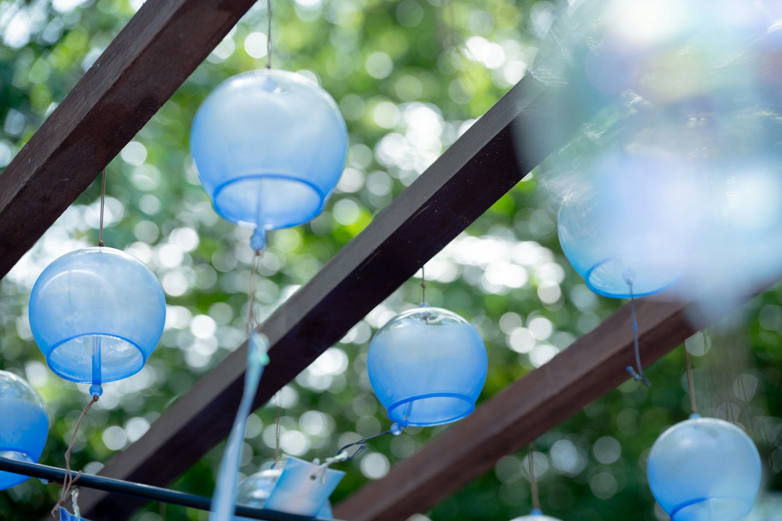 Blaue Laternen hängen unter einer Holzstruktur mit verschwommenem grünem Hintergrund