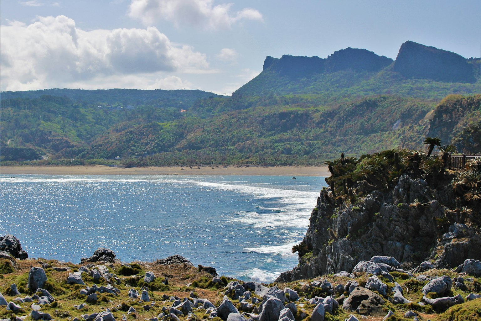 Garis pantai yang indah dengan latar depan berbatu dan laut biru di depan gunung hijau