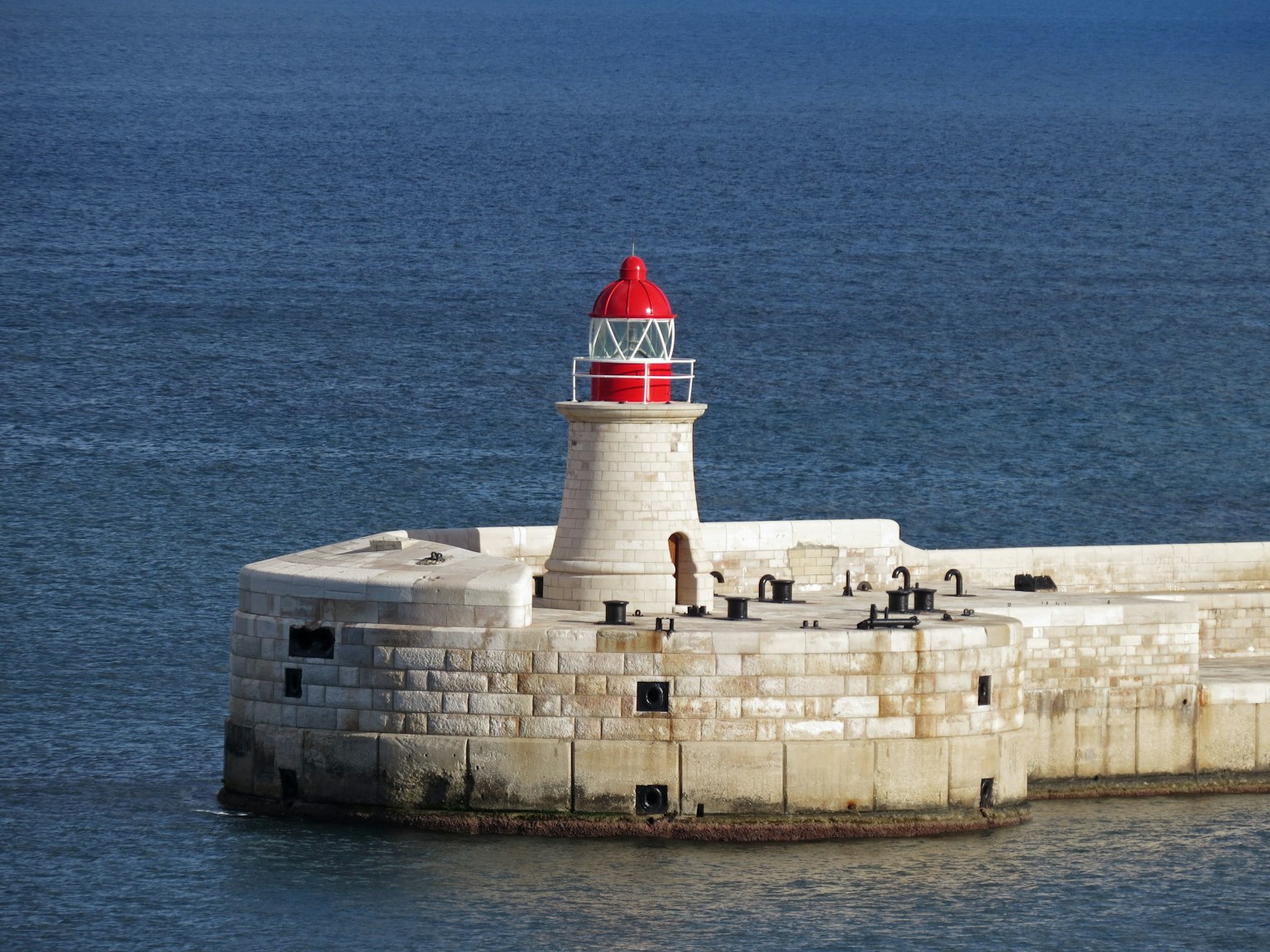 Faro con cima rossa su un molo di pietra al mare