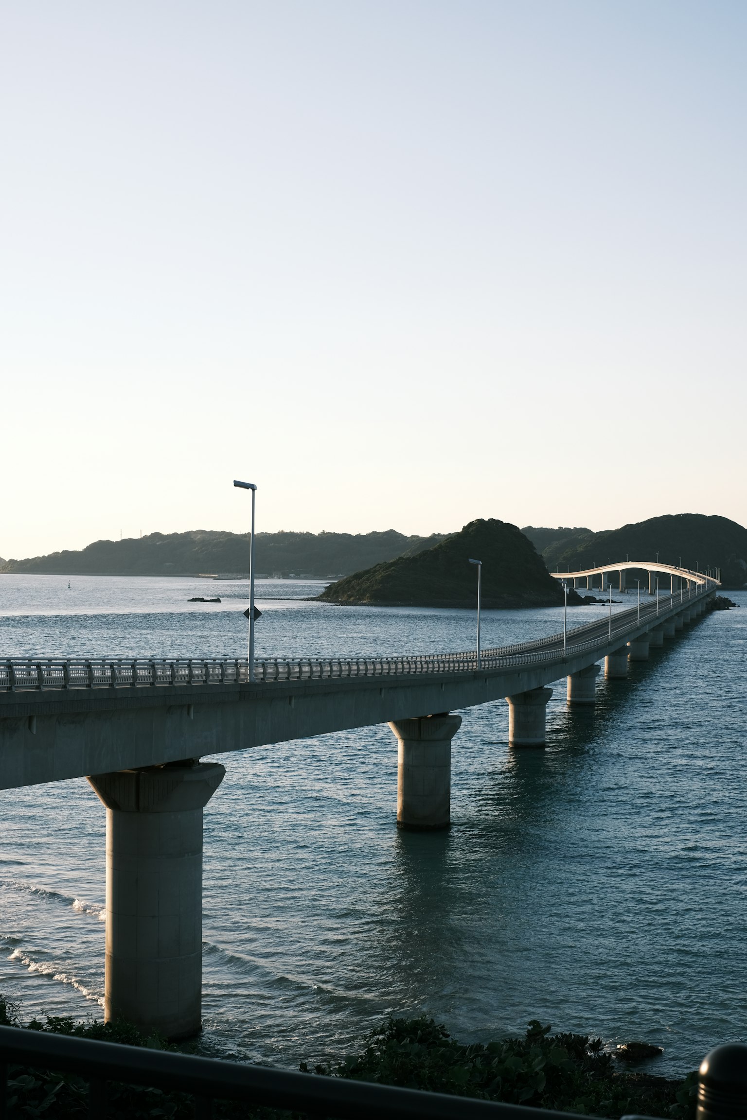 ทิวทัศน์ของสะพานเหนือทะเลในยามพระอาทิตย์ตกพร้อมเกาะอยู่เบื้องหลัง