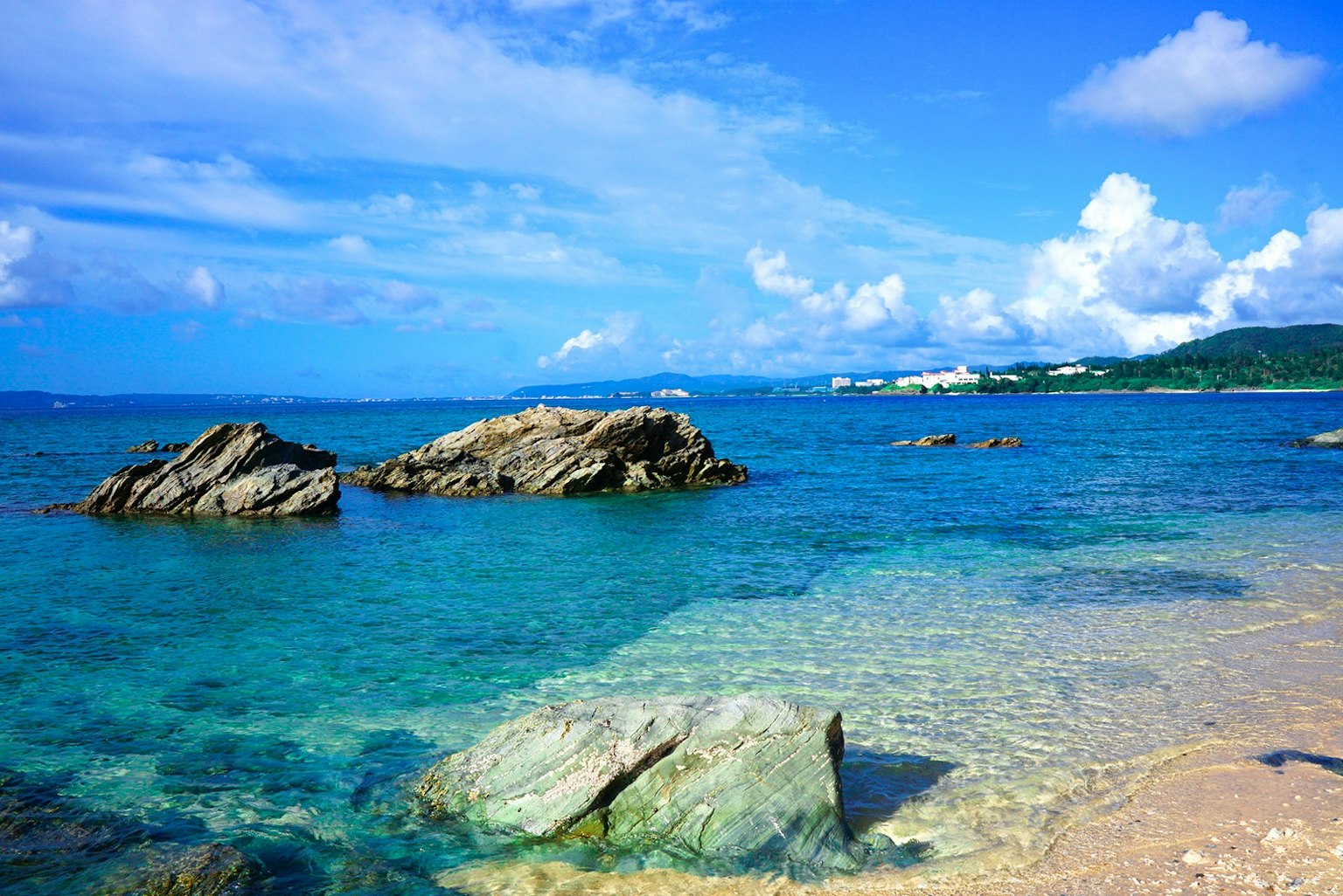 一個風景如畫的海灘景觀，藍色的水和白色的雲，散落著岩石