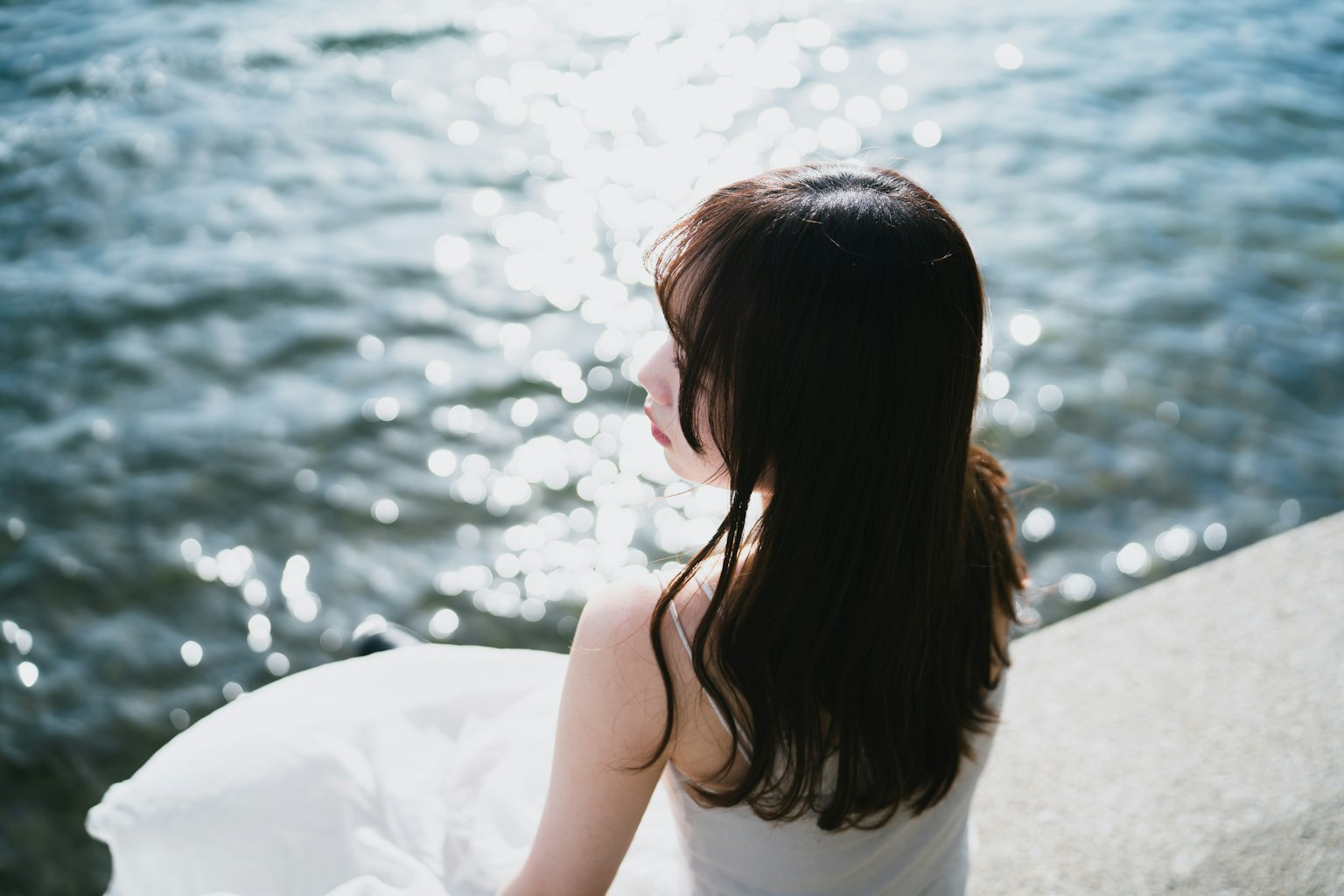 Femme assise près de l'eau avec la lumière du soleil se reflétant sur la surface