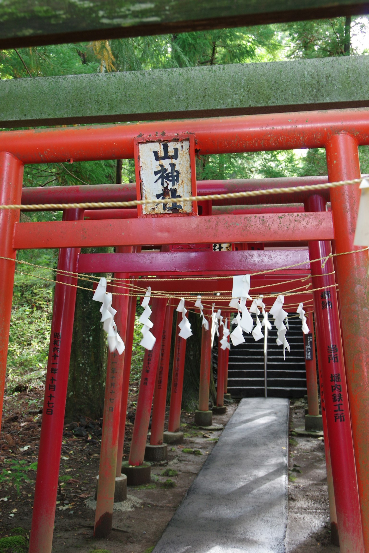 Entrada a un santuario con torii rojos y un cartel con omamori blancos
