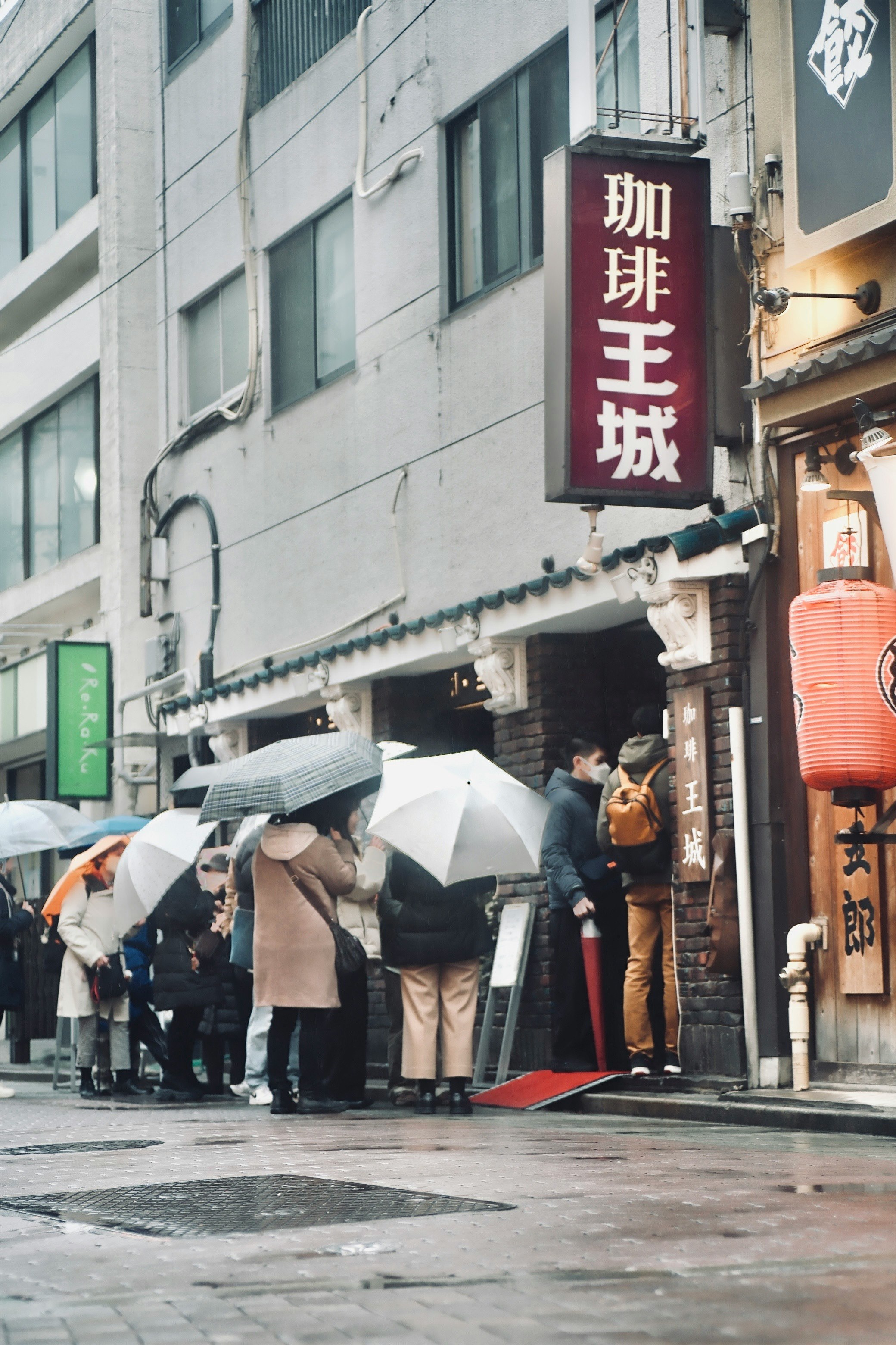 雨上がりの路地で傘をさす人々と看板のある商店街の軒先