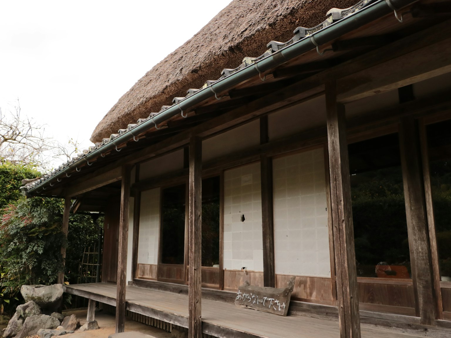 Außenansicht eines traditionellen japanischen Hauses mit Reetdach, das Holzsäulen und Schiebetüren zeigt