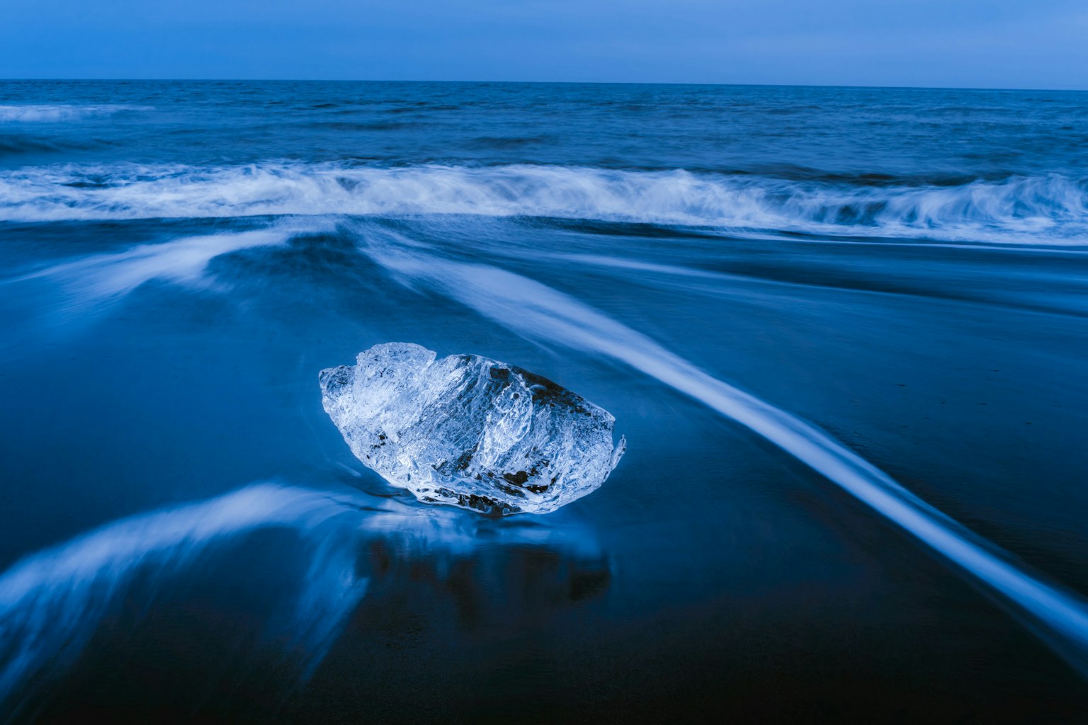 Potongan es transparan di pantai biru dengan gelombang mengalir