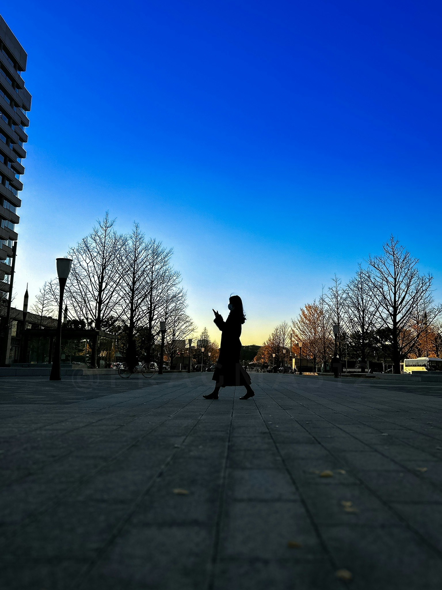 silhouette of a person walking in a plaza under a clear blue sky
