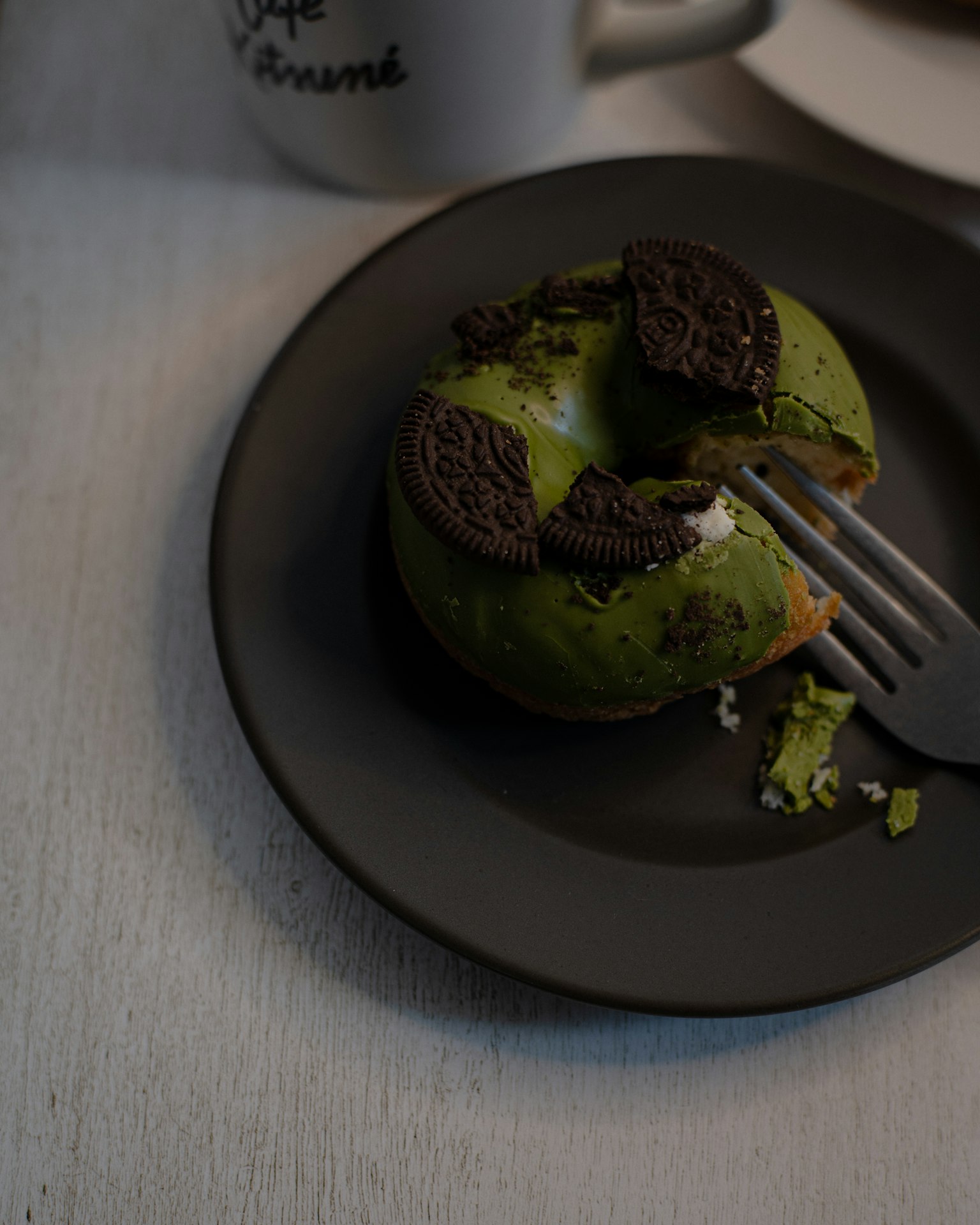 Green donut topped with Oreo cookies on a black plate