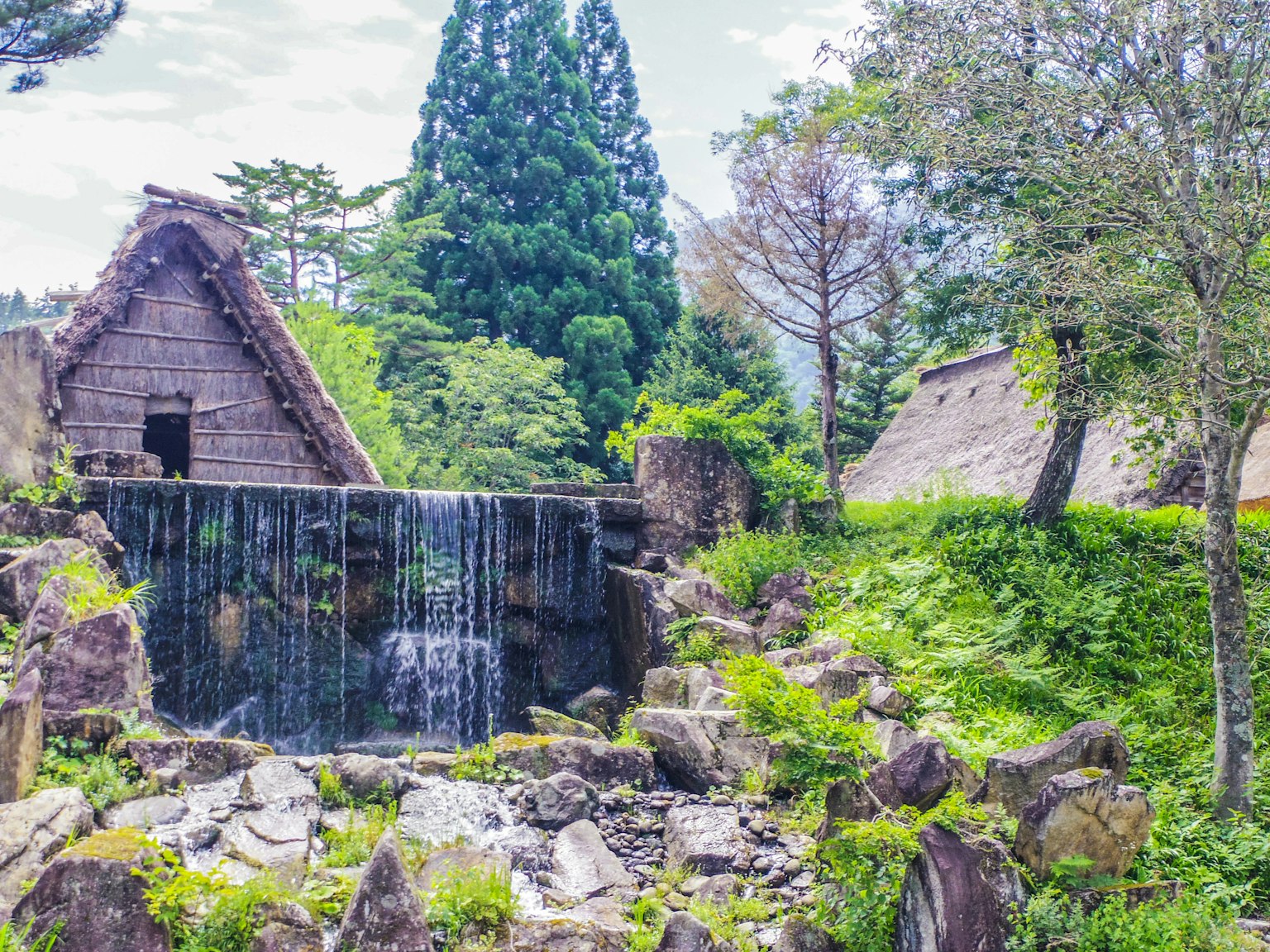 Traditional thatched-roof houses in a beautiful rural Japanese landscape with a small waterfall