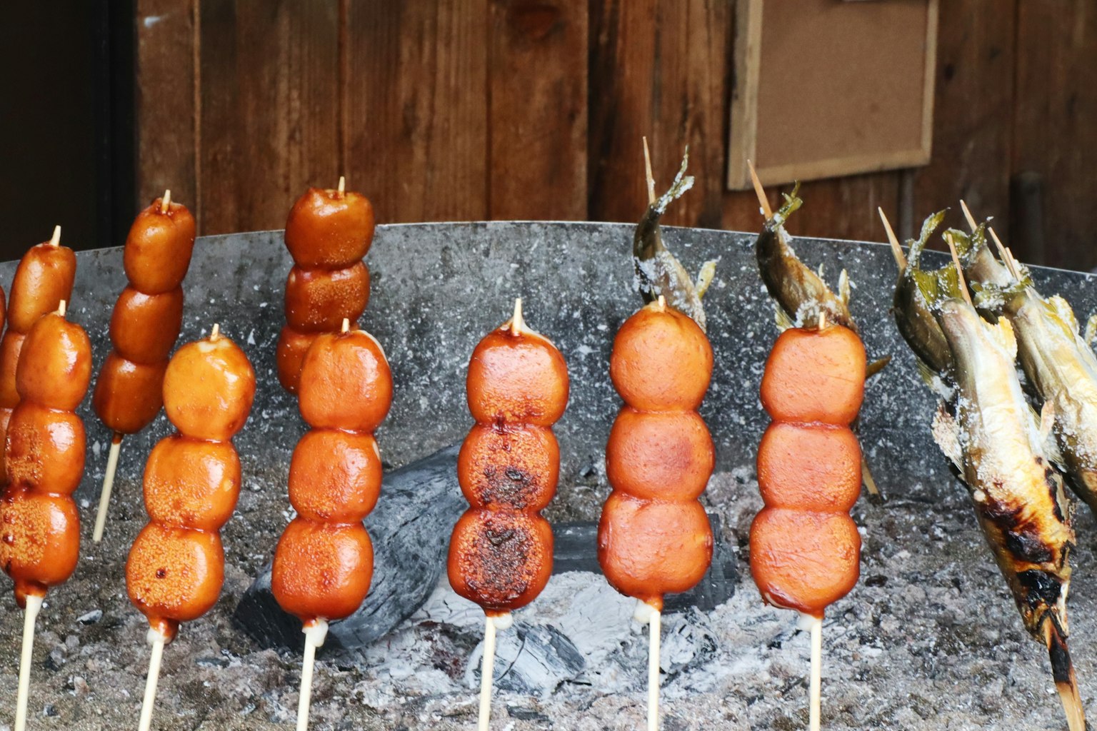 Salchichas a la parrilla en brochetas y pescado cocinándose al carbón