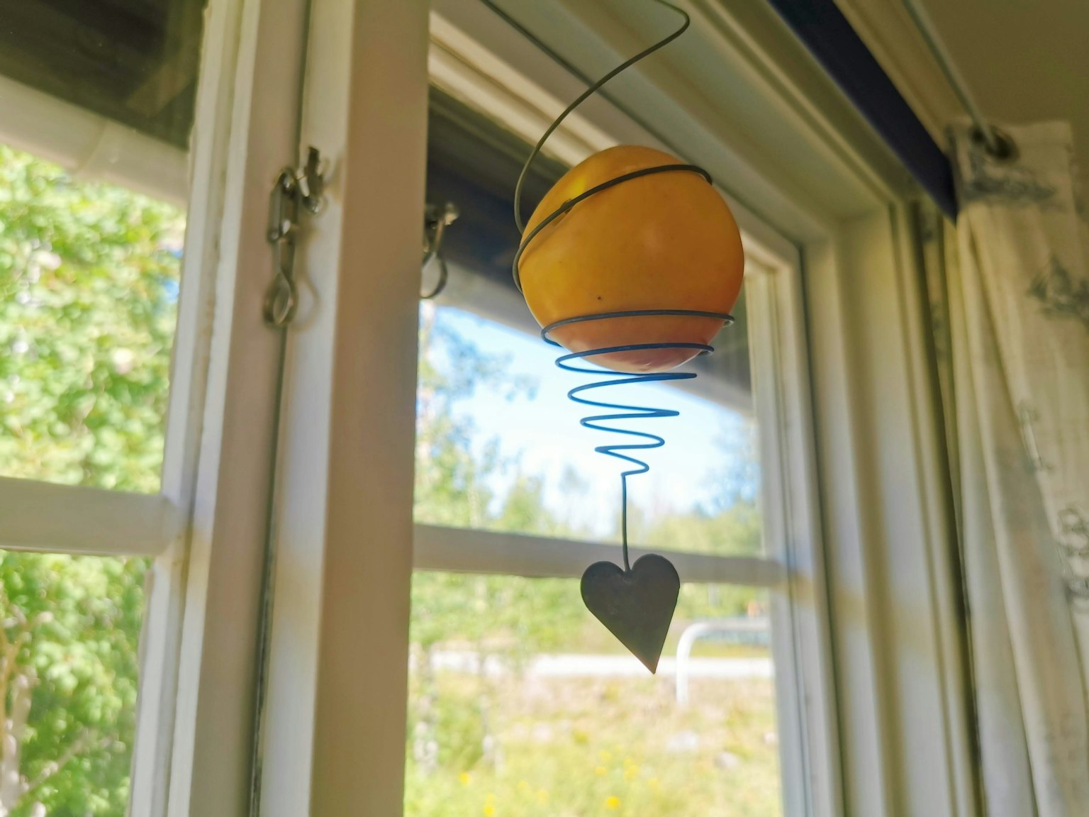 Esfera naranja colgante con decoración en forma de corazón junto a una ventana