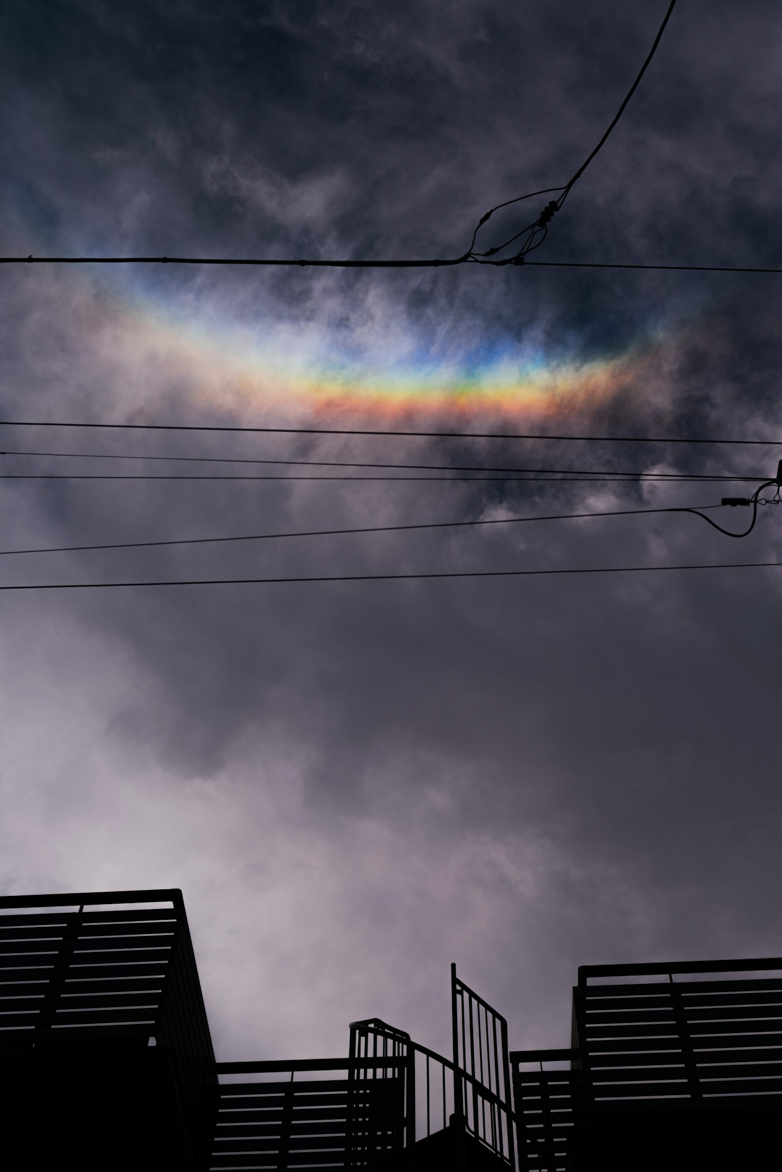 Ein Regenbogenbogen zwischen dunklen Wolken mit Stromleitungen