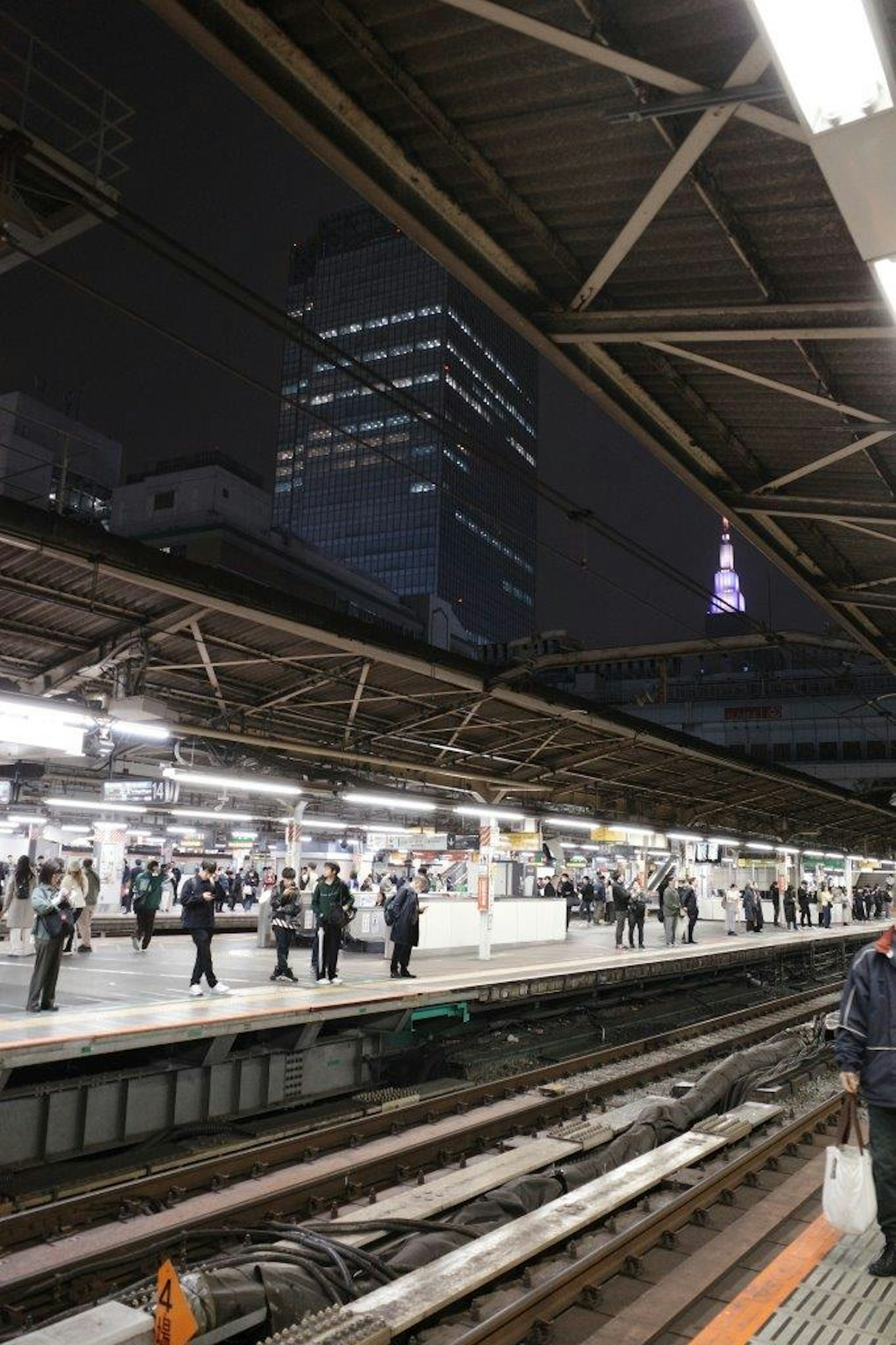 Folla di persone in attesa alla stazione ferroviaria di notte con la Torre di Tokyo sullo sfondo