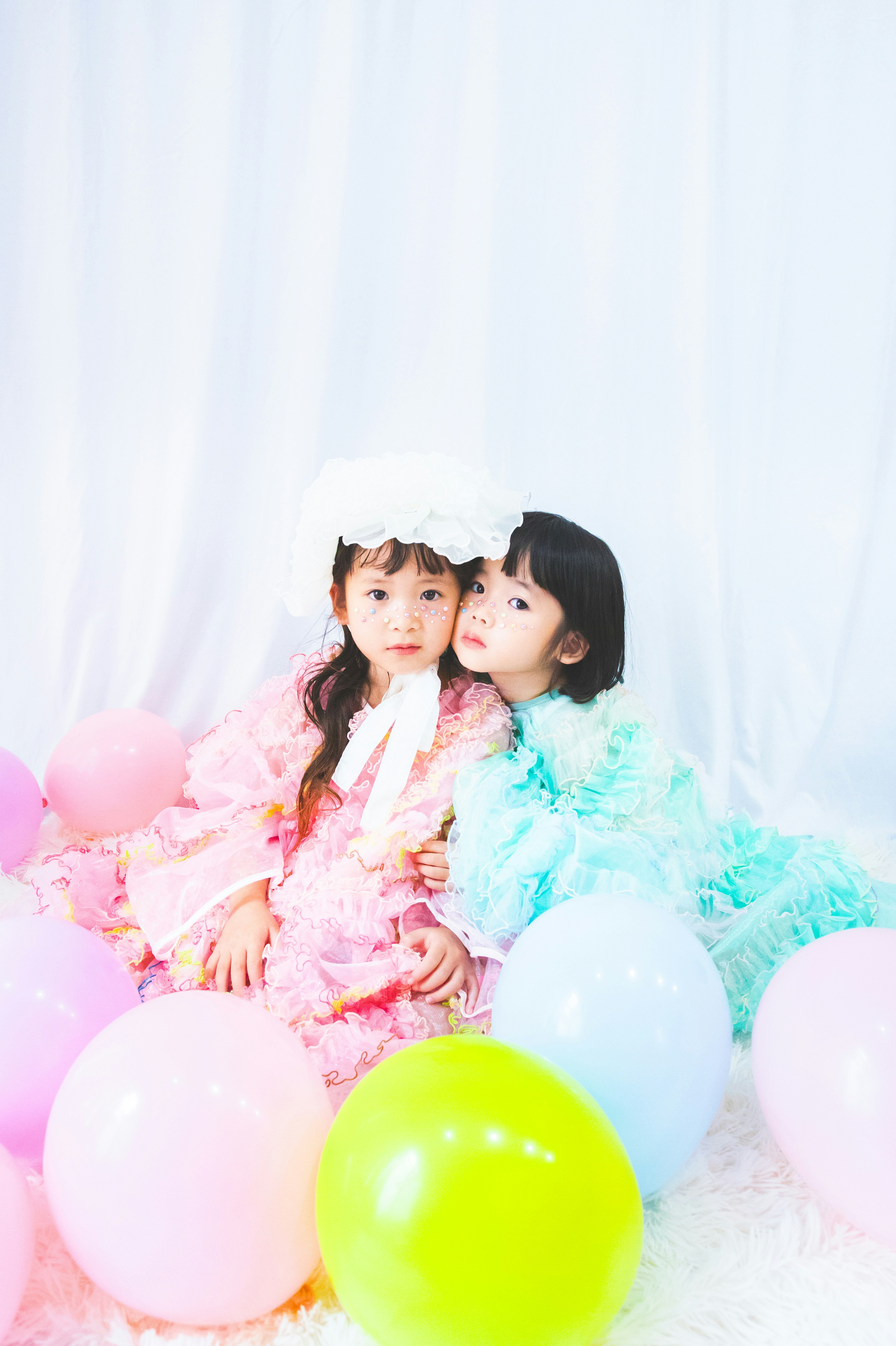 ふわふわのドレスを着た2人の子どもとカラフルな風船のあるスタジオ背景