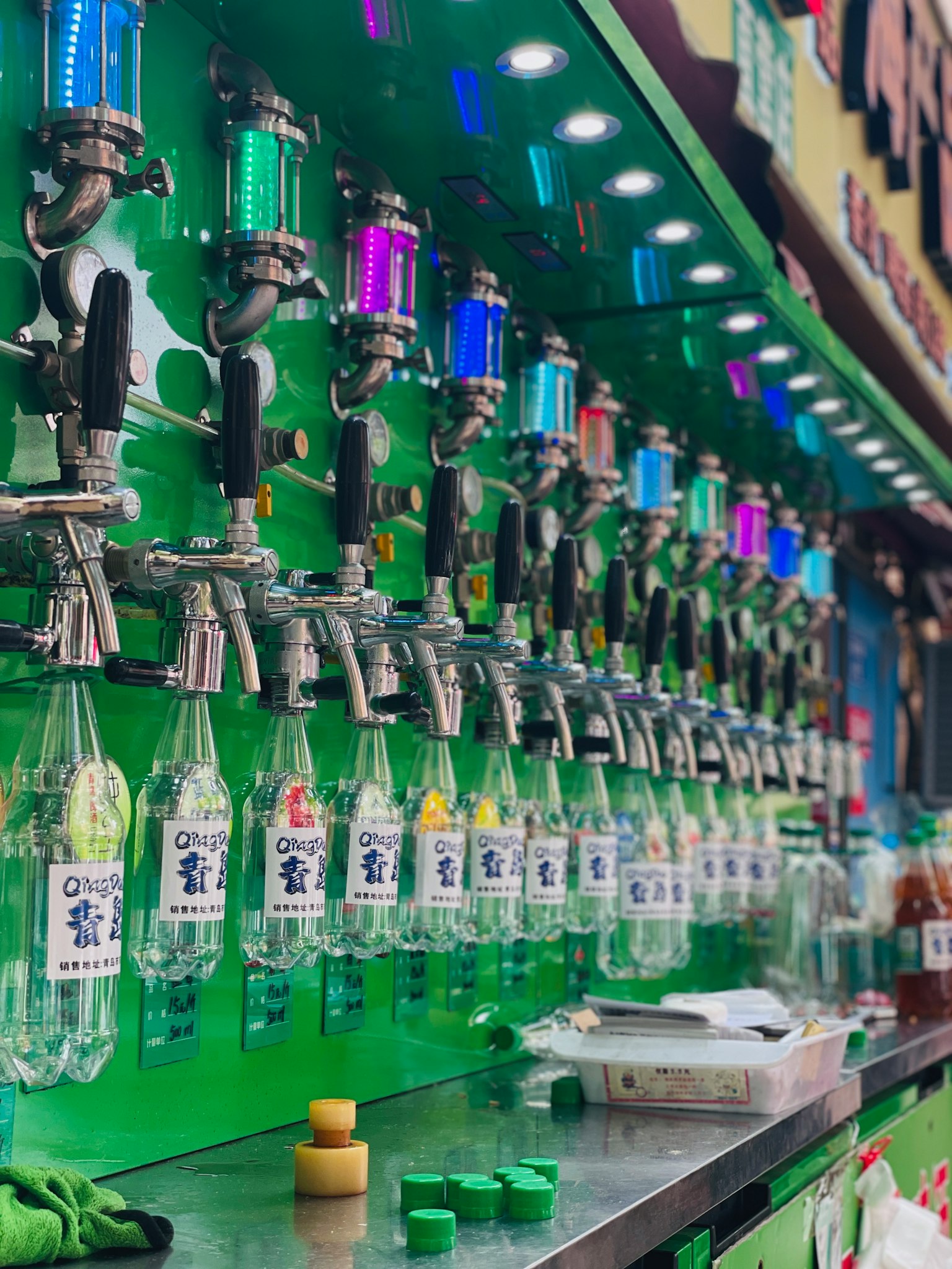 カラフルな飲料ディスペンサーが並ぶ緑の壁の前に置かれた瓶