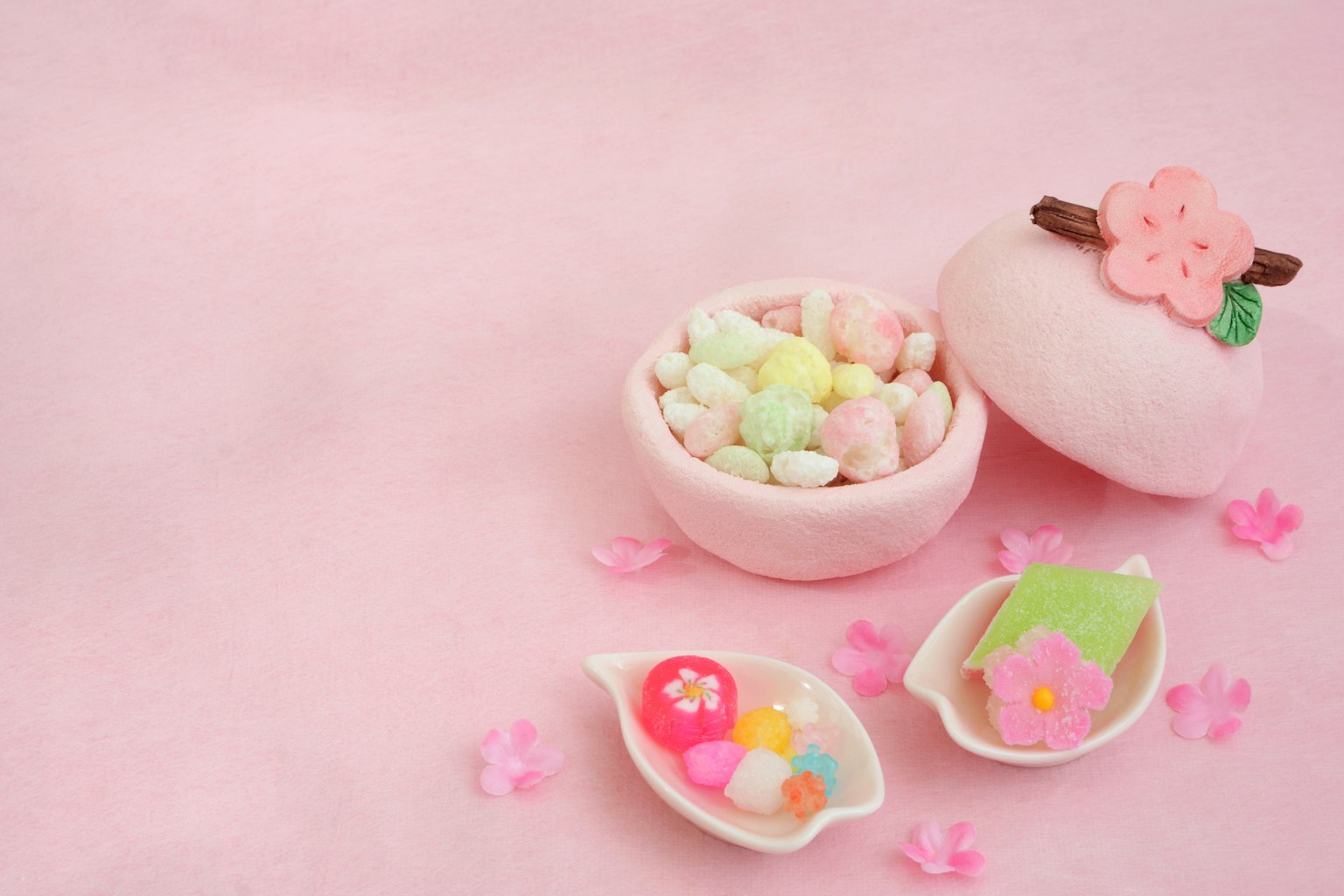Caramelle colorate in una ciotola rosa decorata con fiori di ciliegio su uno sfondo rosa
