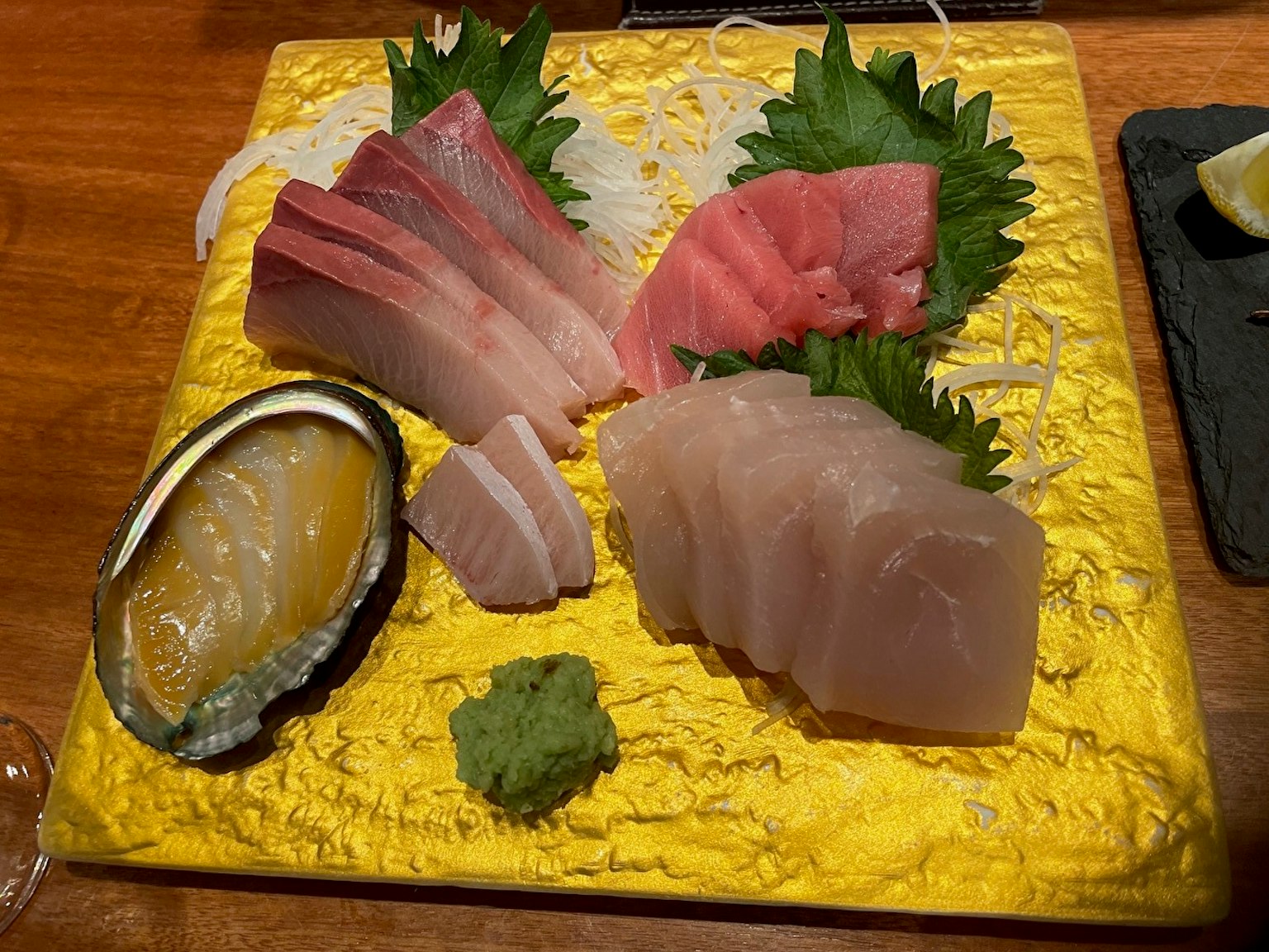 Plato de sashimi fresco servido en un plato dorado con wasabi