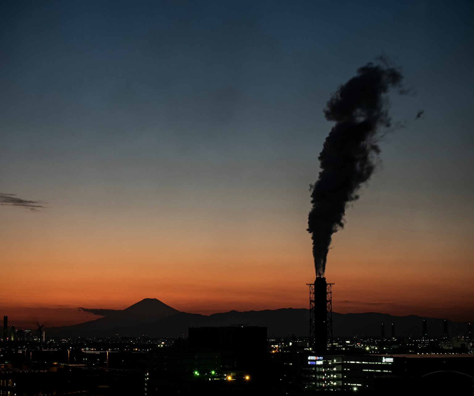 夕陽下，富士山與冒煙煙囪的輪廓
