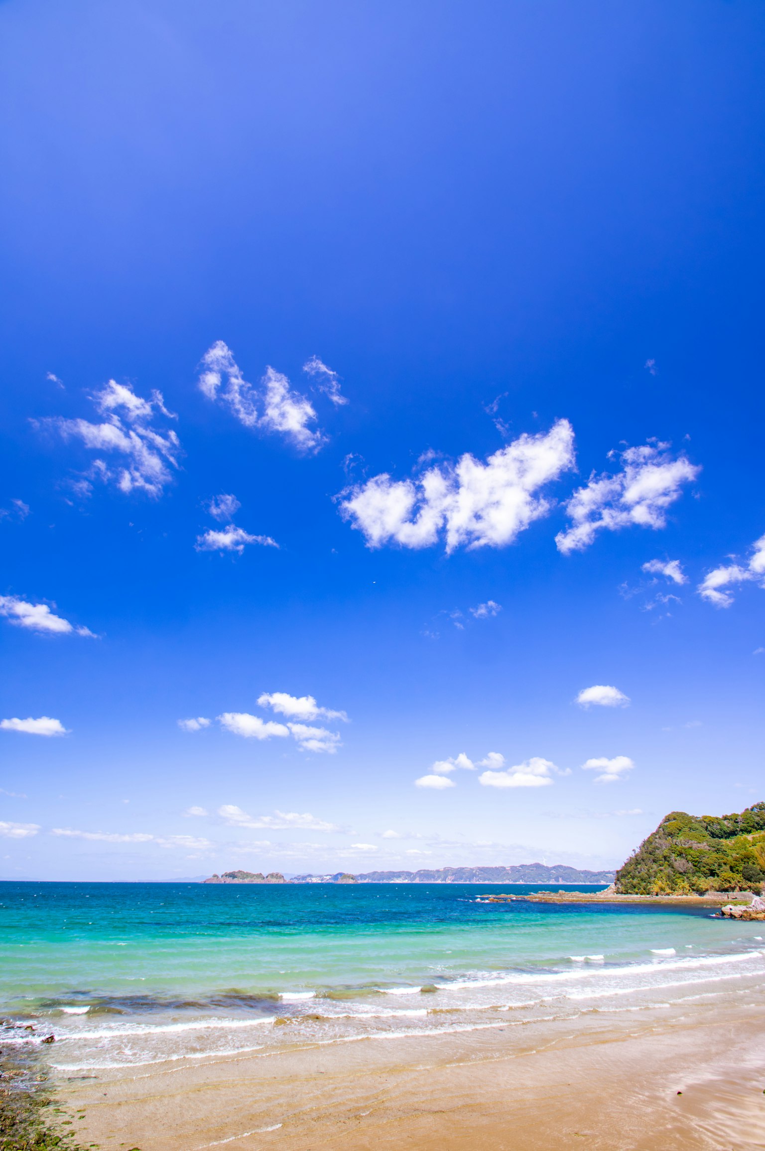 A beach scene with a blue sky and white clouds turquoise water and sandy shore