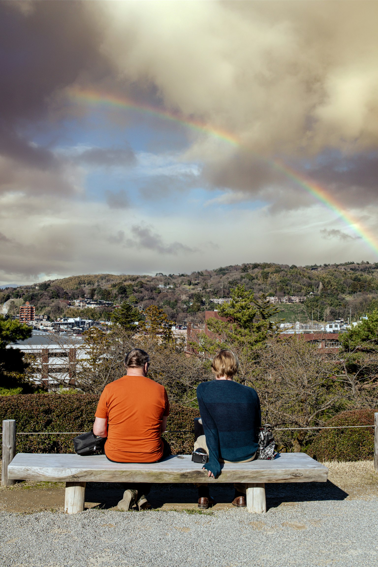 兩個人坐在長椅上,身處彩虹下,俯瞰風景