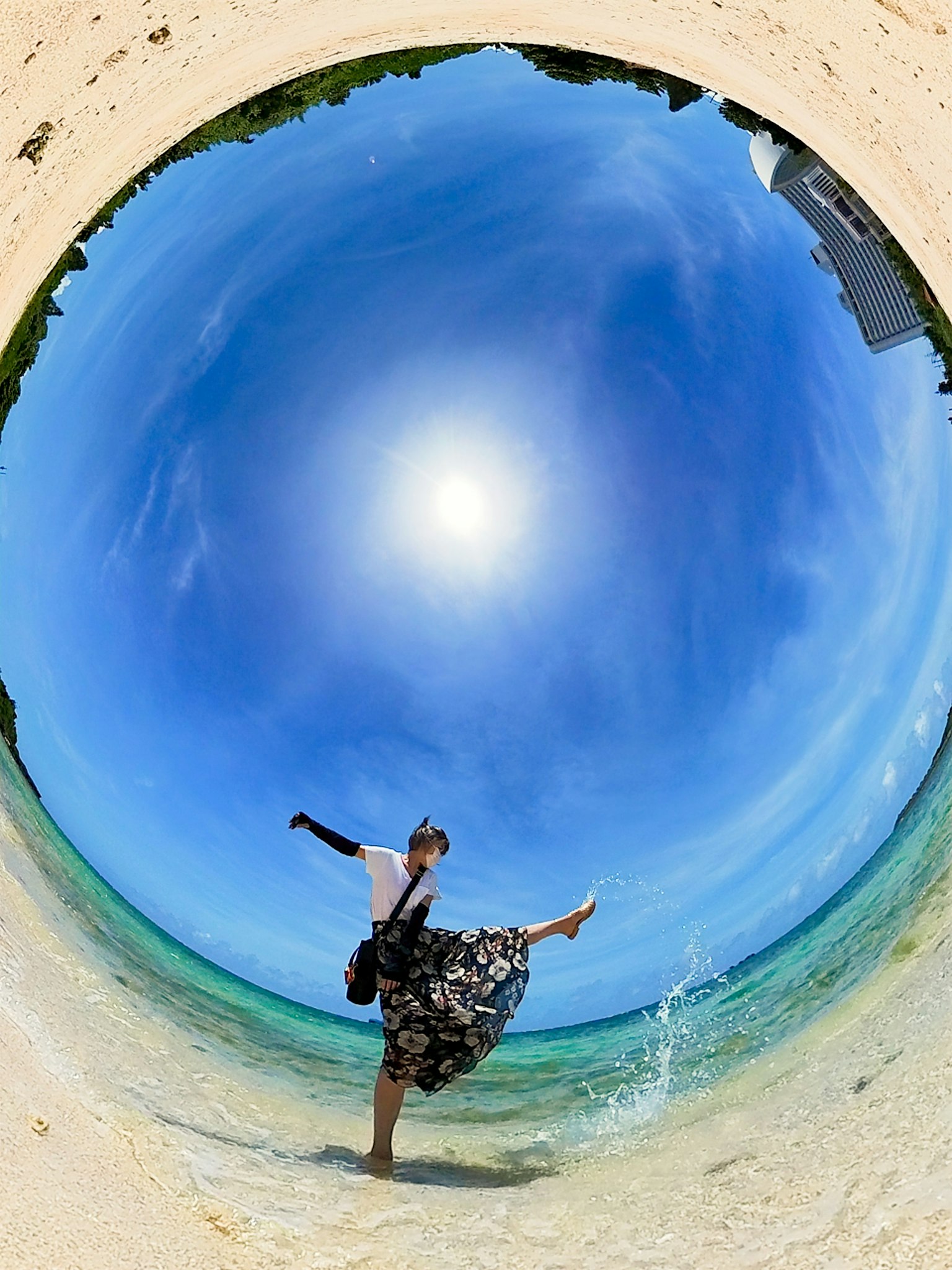 Une vue panoramique d'une femme dansant sur une plage sous un ciel bleu et un soleil