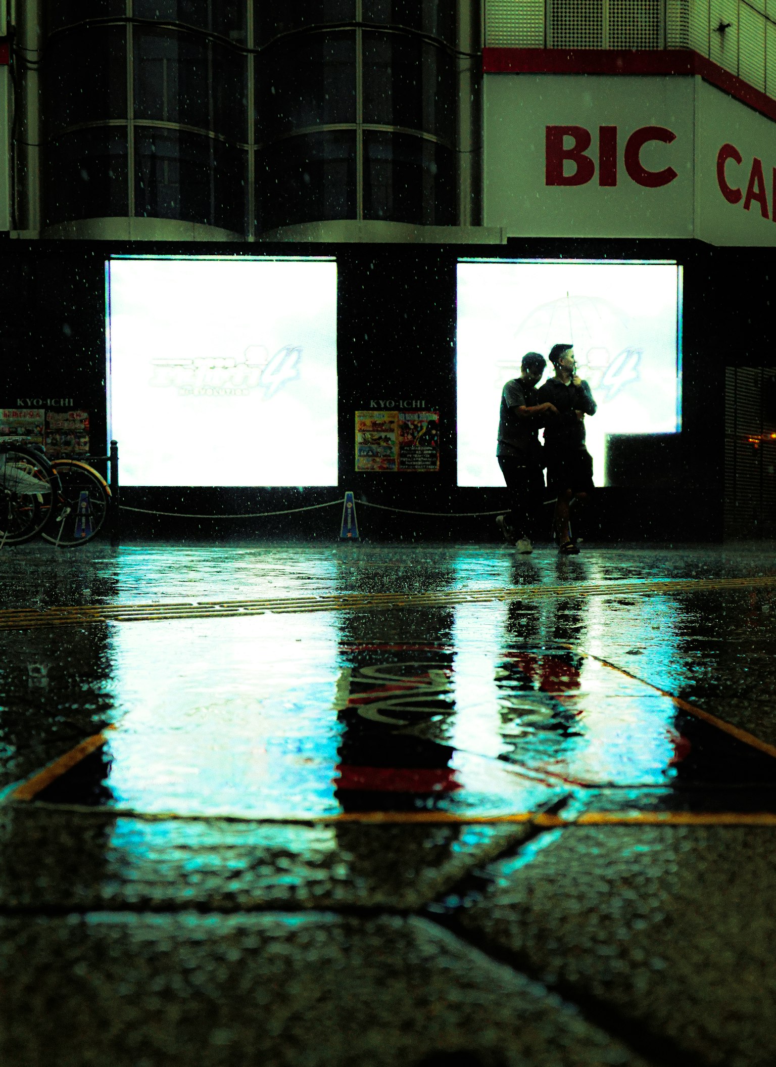 Two people standing in the rain with glowing reflections in an urban scene