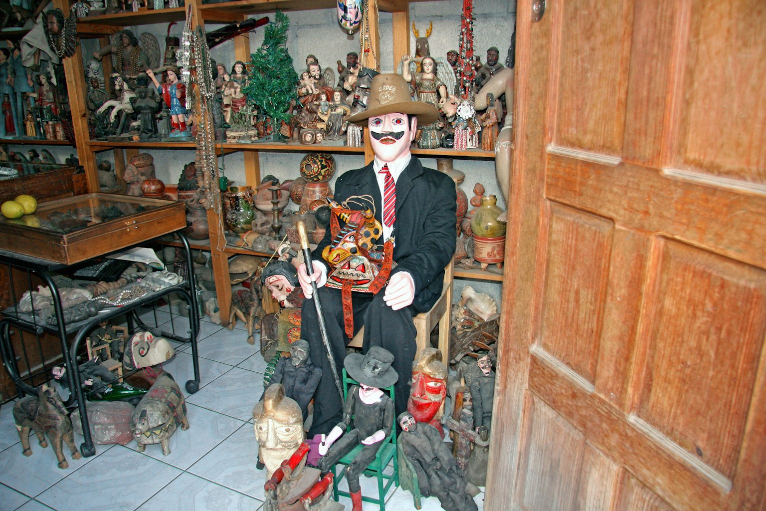 Una muñeca vestida con traje y sombrero sentada entre varias figuras de madera