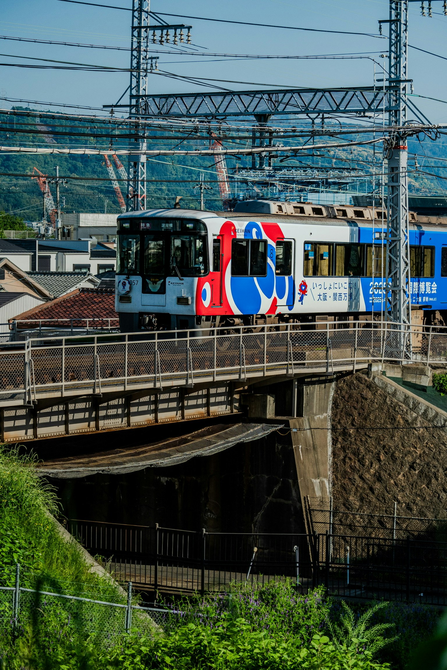 Bunter Zug überquert eine Brücke mit industriellem Hintergrund