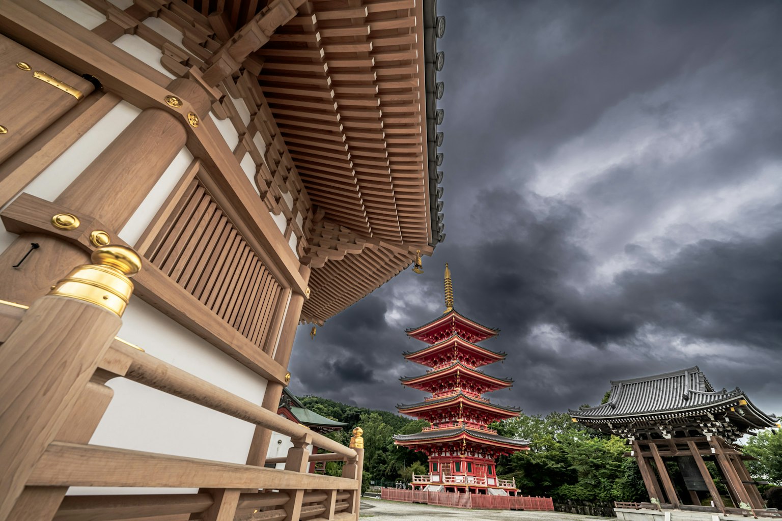Pagoda roja de cinco pisos junto a una arquitectura de madera bajo un cielo nublado oscuro