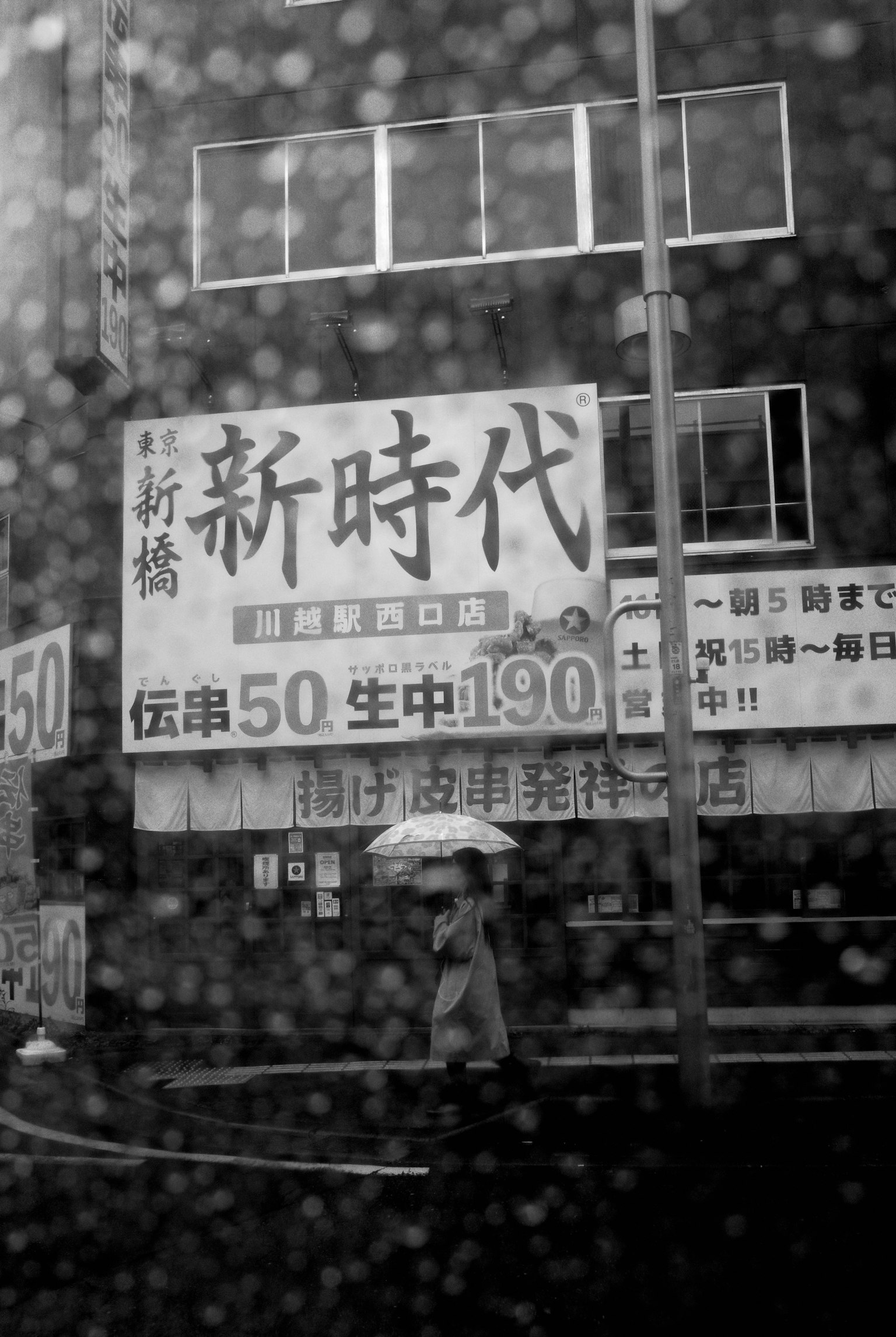 一个黑白城市景观，有一个人撑着伞走路和一个写着新时代理念的标志